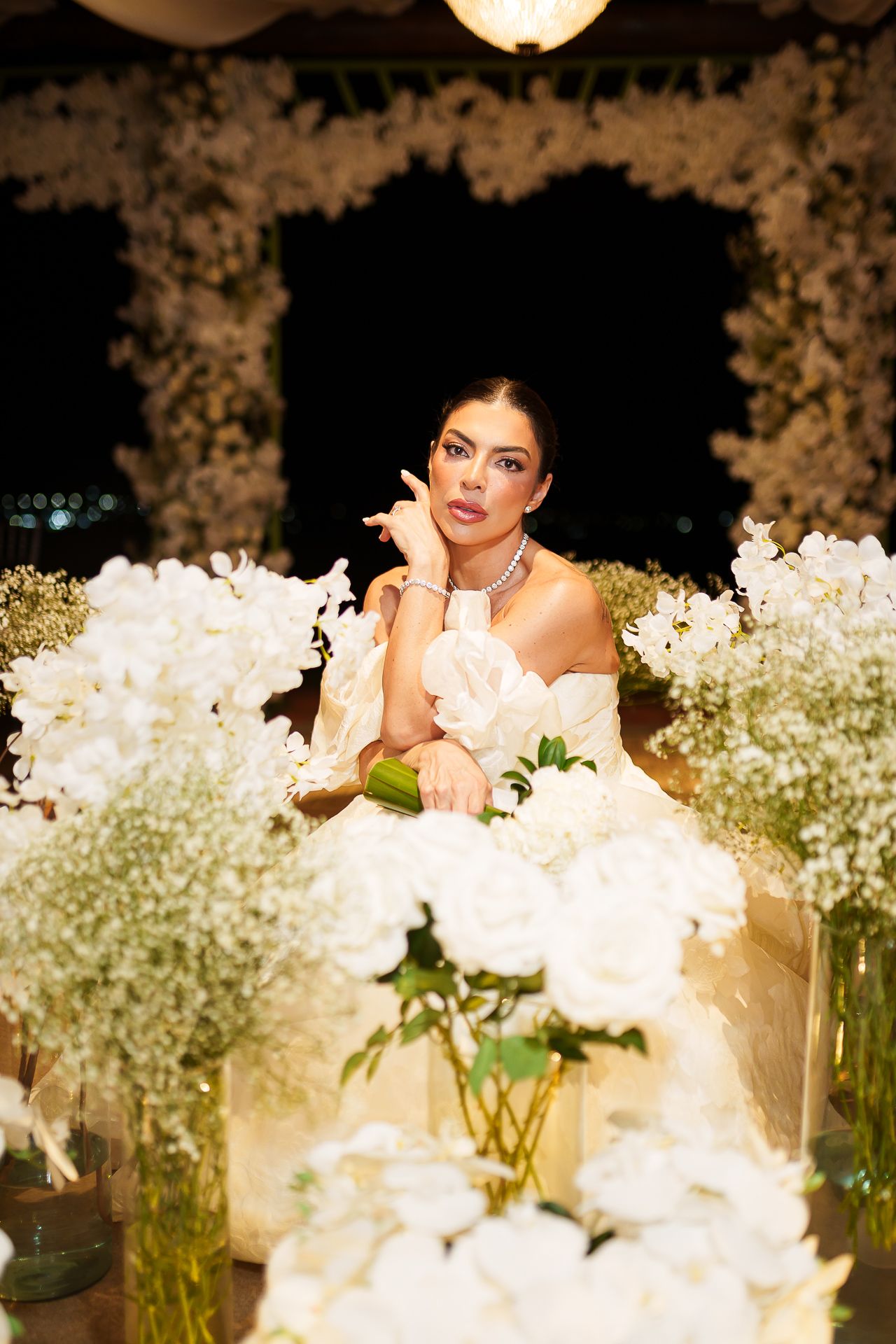 Elegant bride in white gown surrounded by lush white floral arrangements at a luxurious wedding reception.