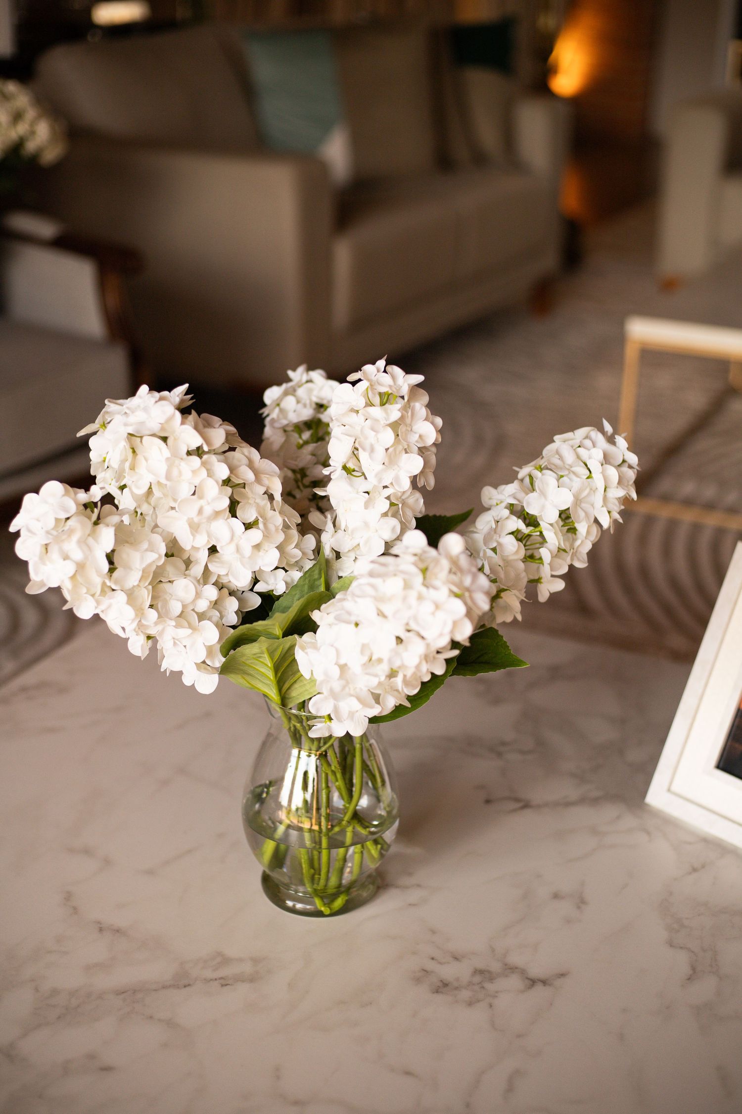 White hydrangea bouquet in a clear glass vase on a marble table in an elegant living room.