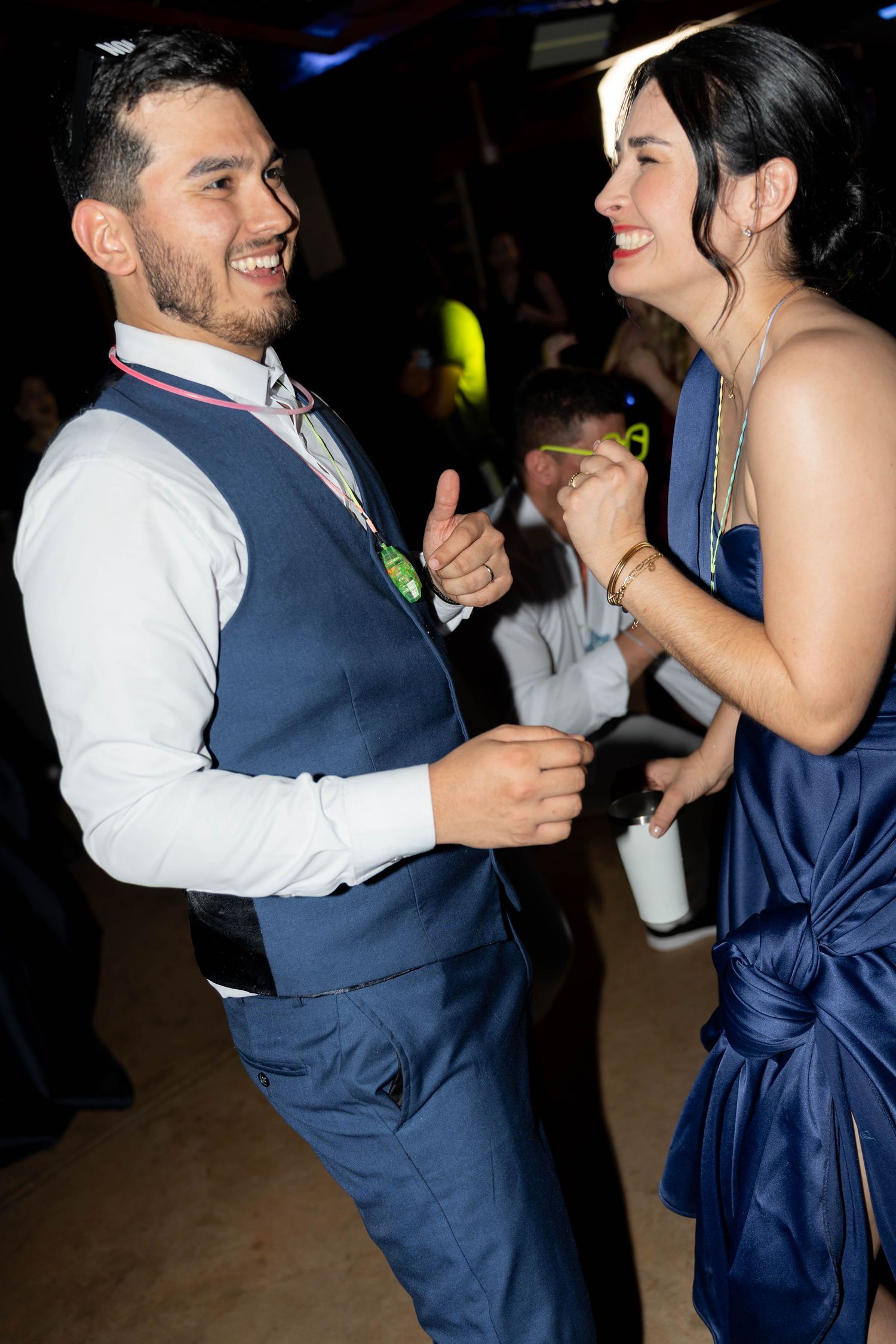 A man in a blue vest and woman in a navy dress smile and dance together at a formal event.