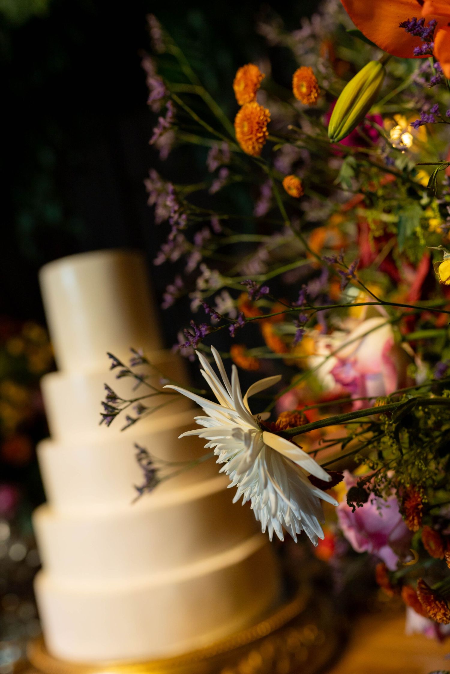 Elegant white tiered wedding cake with bird silhouettes beside vibrant orange and purple floral arrangement.