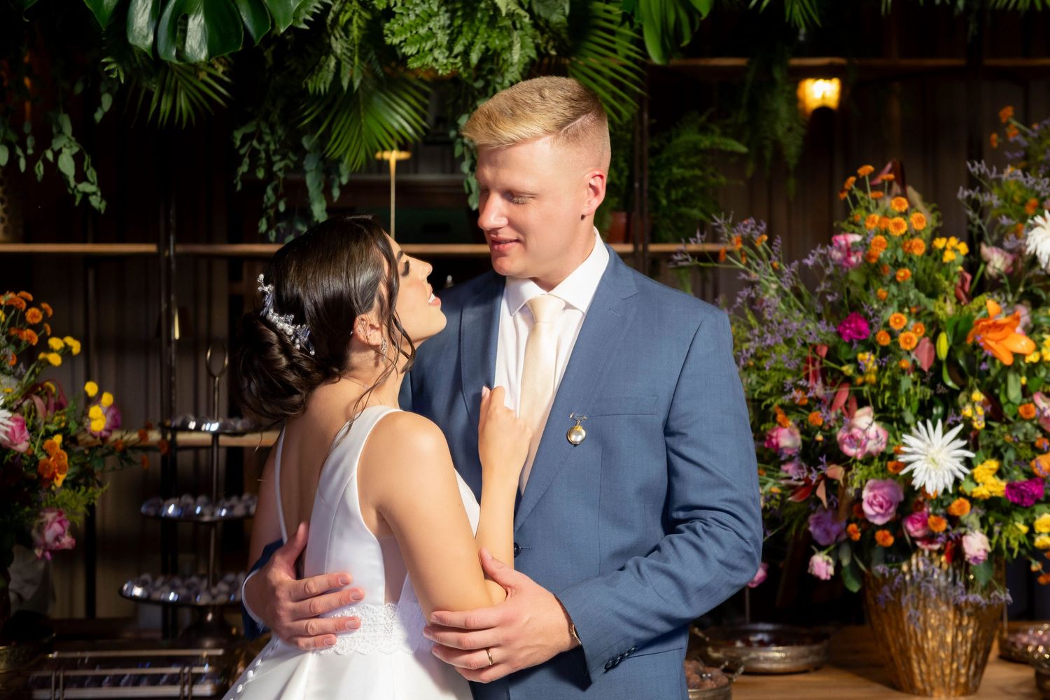Bride and groom share a tender dance moment surrounded by lush greenery and colorful floral arrangements.