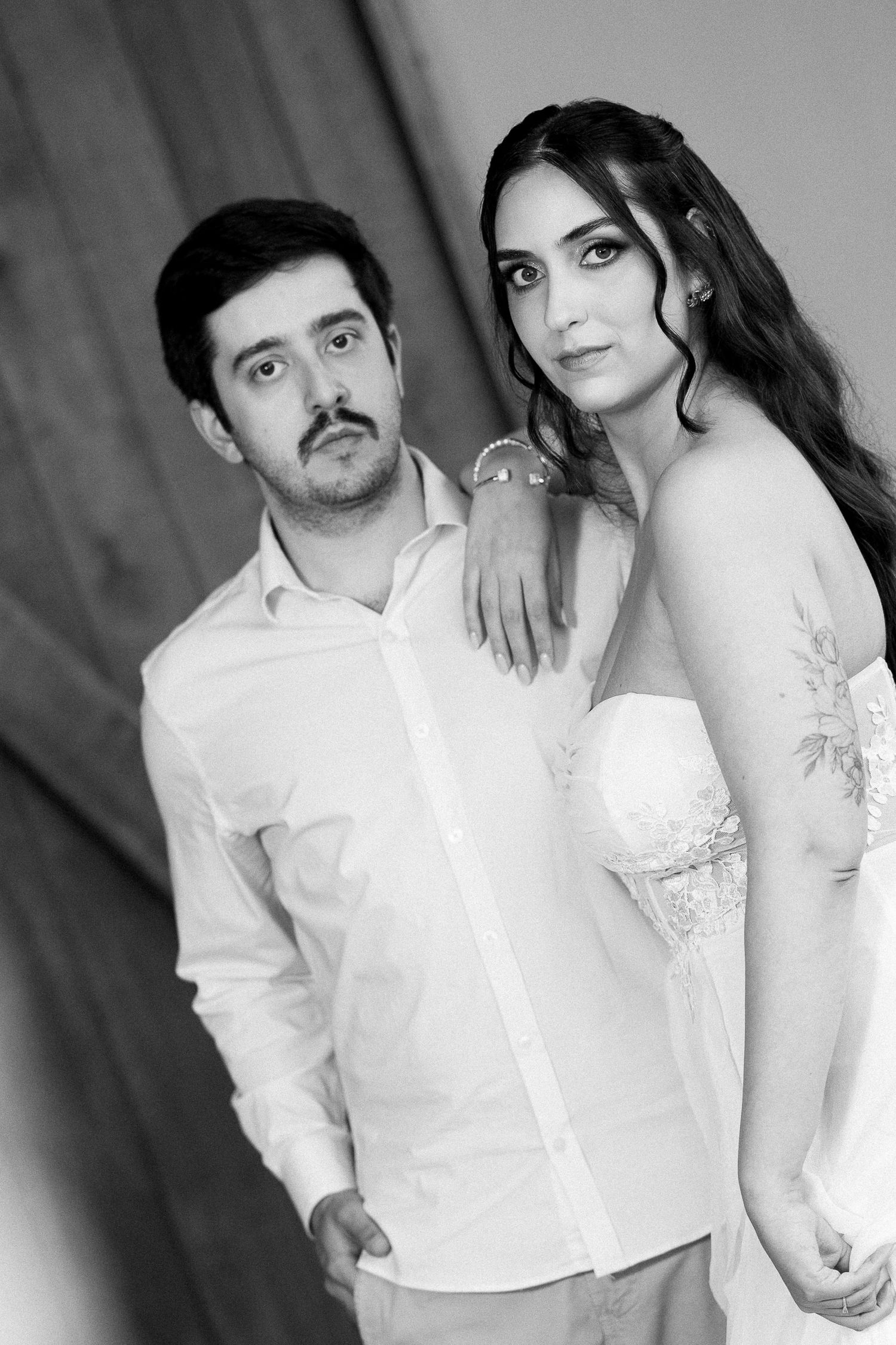 Black and white portrait of a couple, woman in strapless gown resting arm on mans shoulder in white shirt.