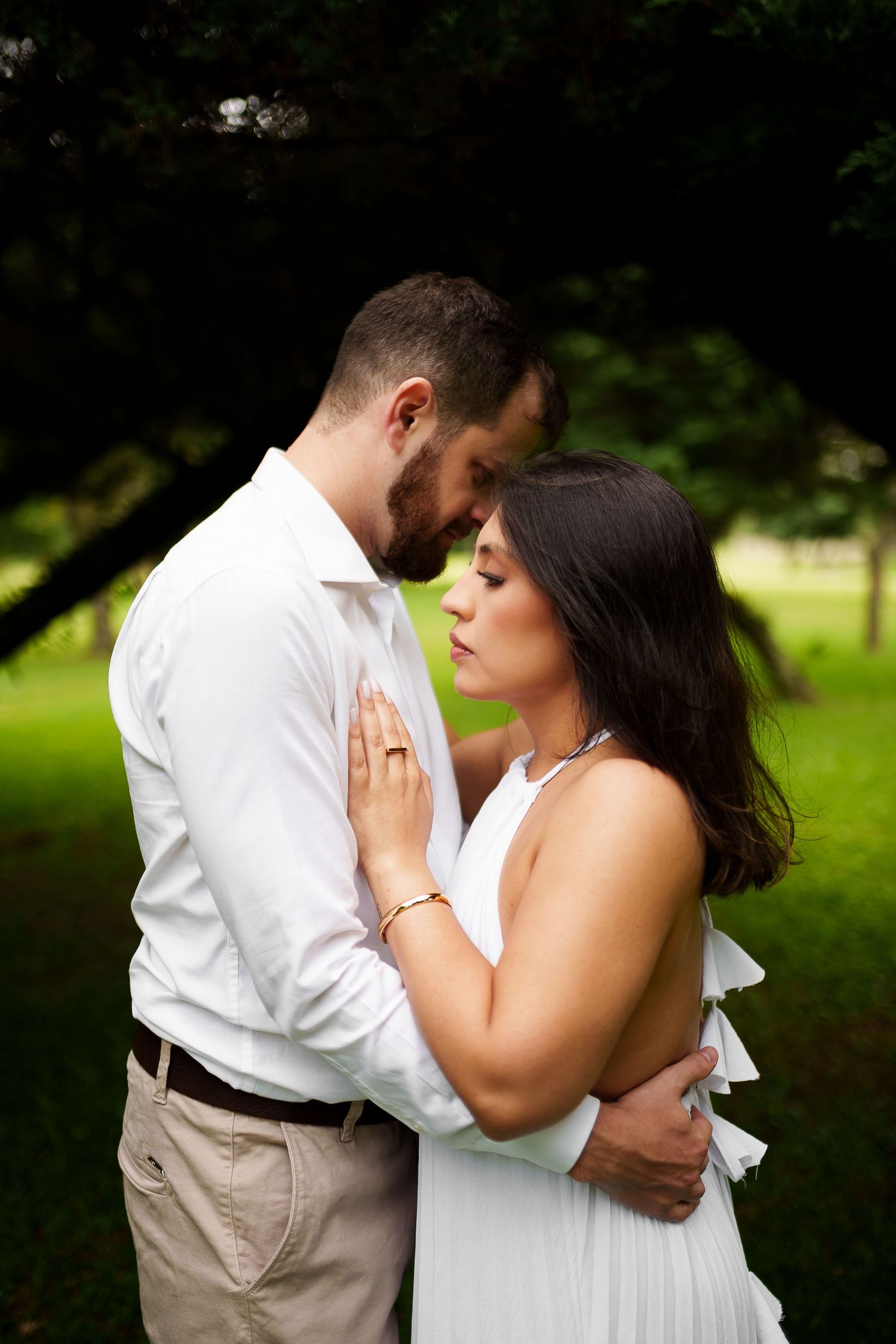 Couple in white outfits sharing a tender embrace in a lush green park setting.