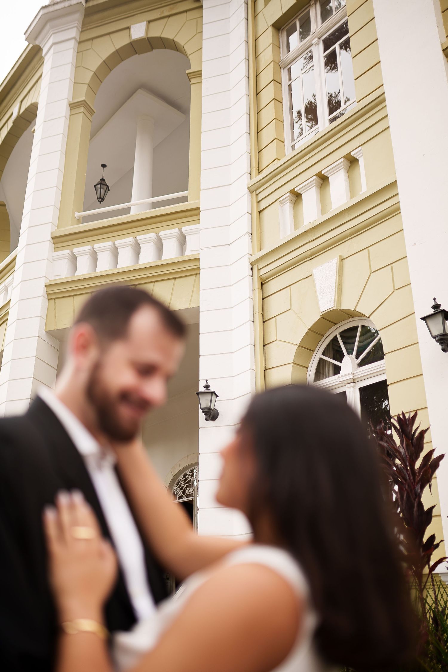 Bride and groom share a romantic moment outside an elegant yellow and white colonial building.