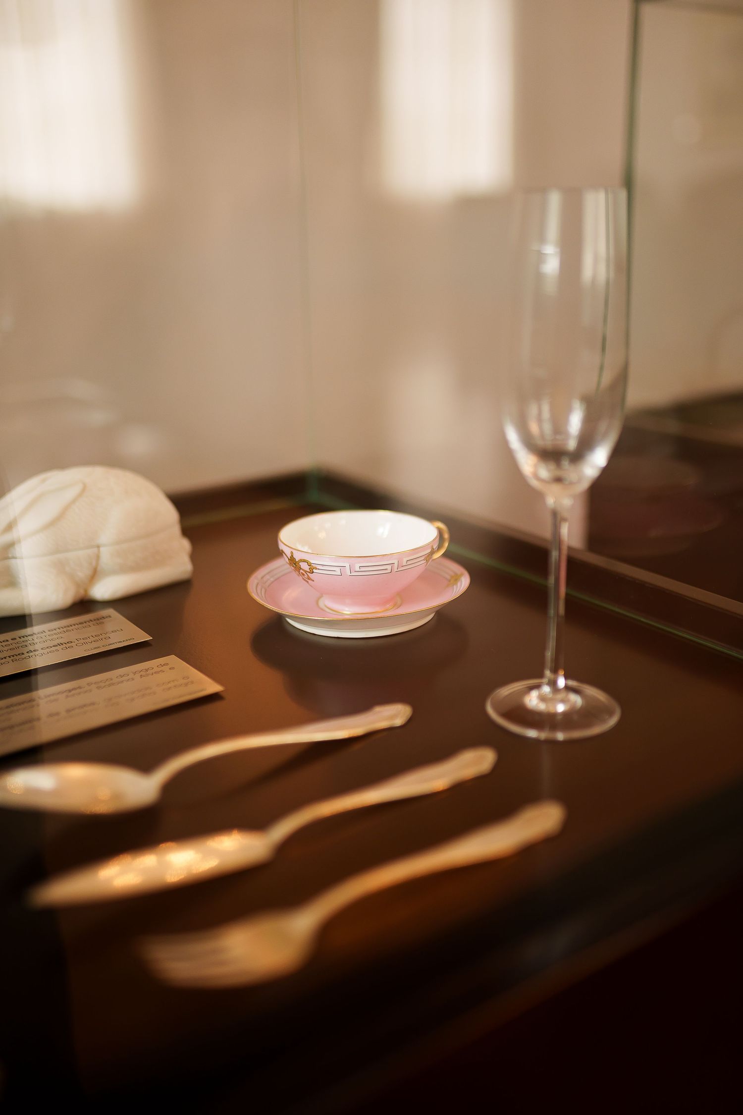 Elegant table setting with pink teacup on saucer, crystal champagne flute, and gold cutlery on dark wooden tray.
