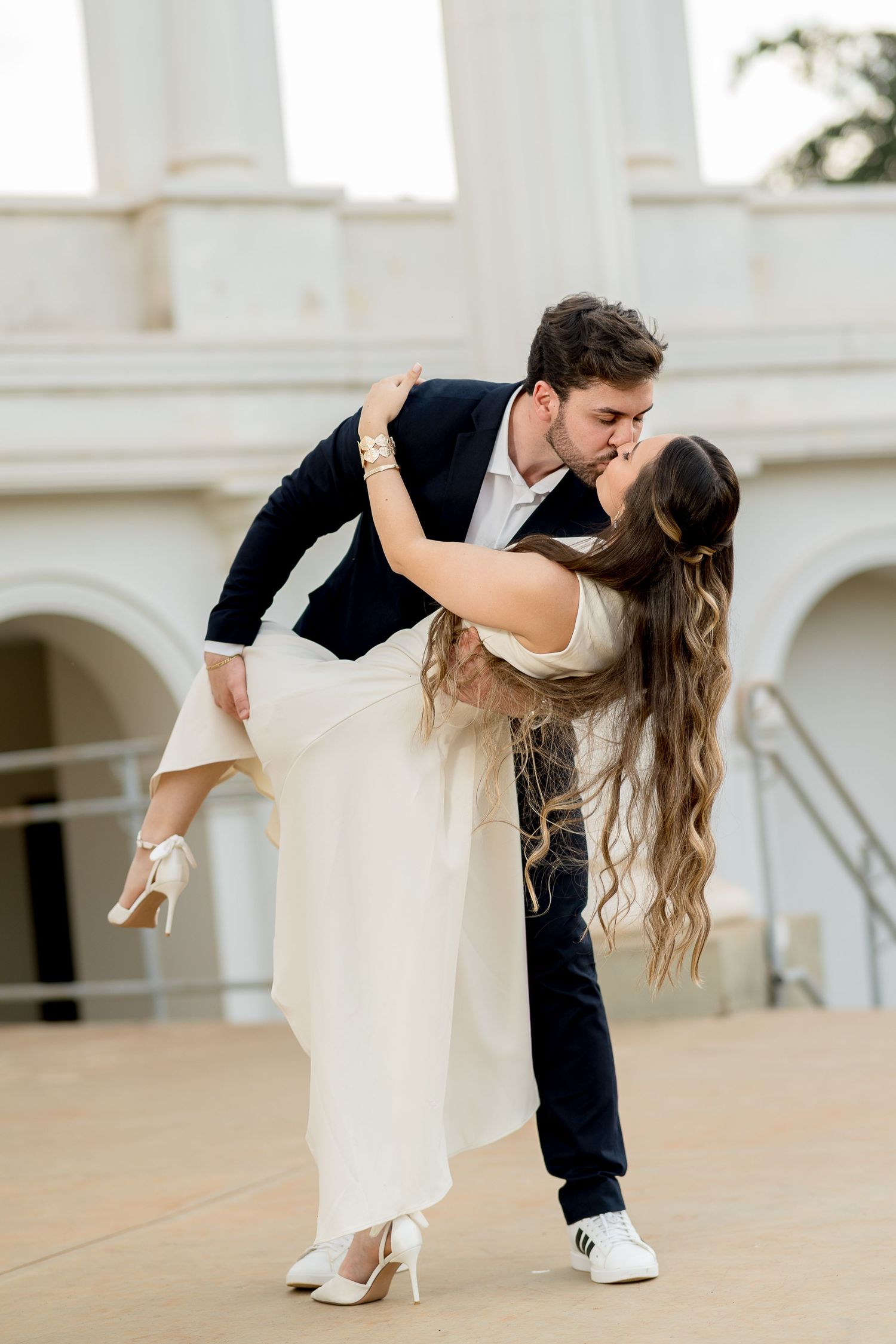 Couple sharing a romantic dip kiss outdoors, groom in black suit, bride in white dress with long flowing hair.