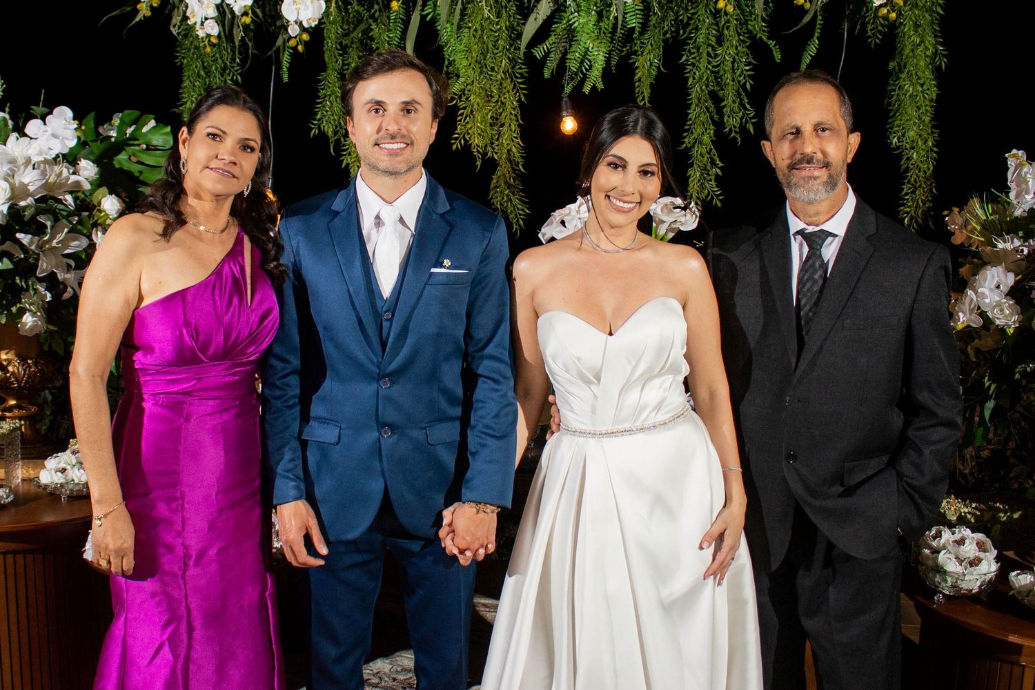 A bride and groom pose with family members in formal attire at an elegant floral wedding reception.