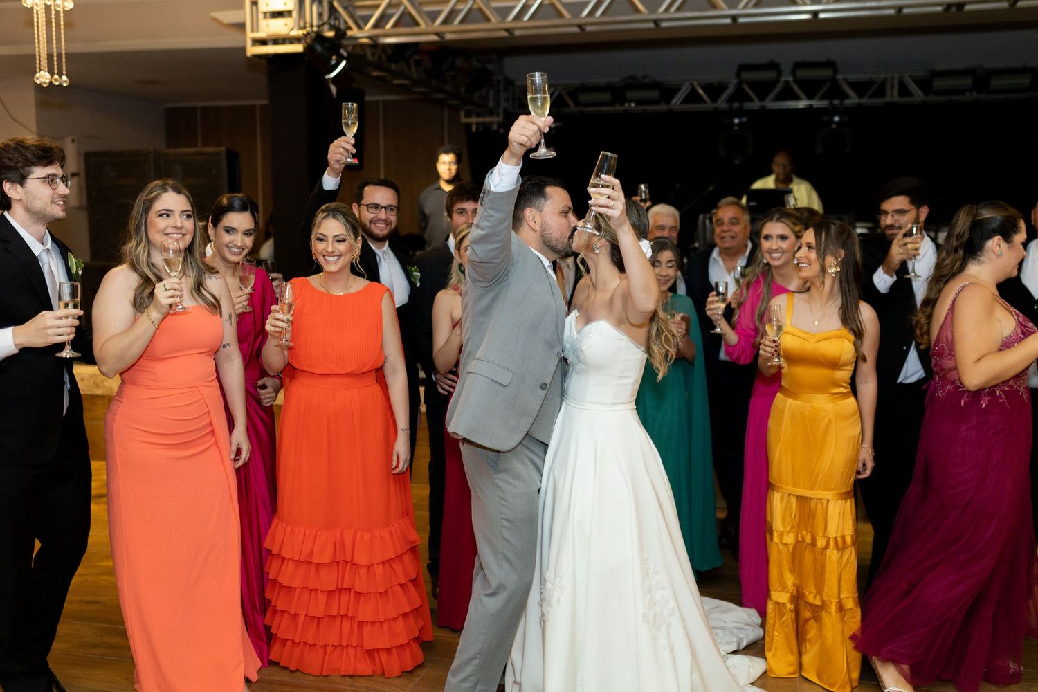 Bride and groom kissing while wedding guests raise champagne glasses in celebration on the dance floor.