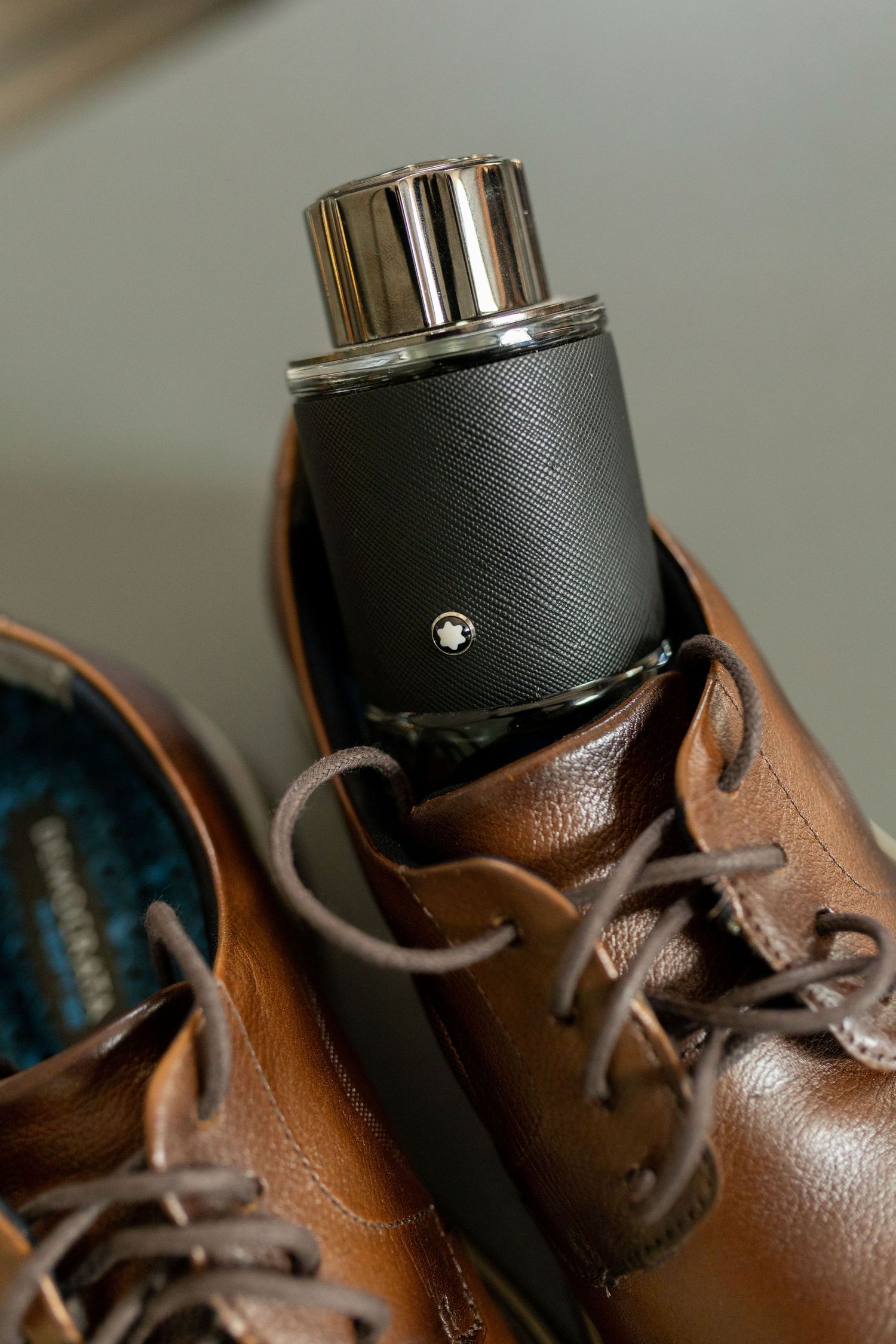 Montblanc cologne bottle placed between tan leather lace-up dress shoes on a gray surface.