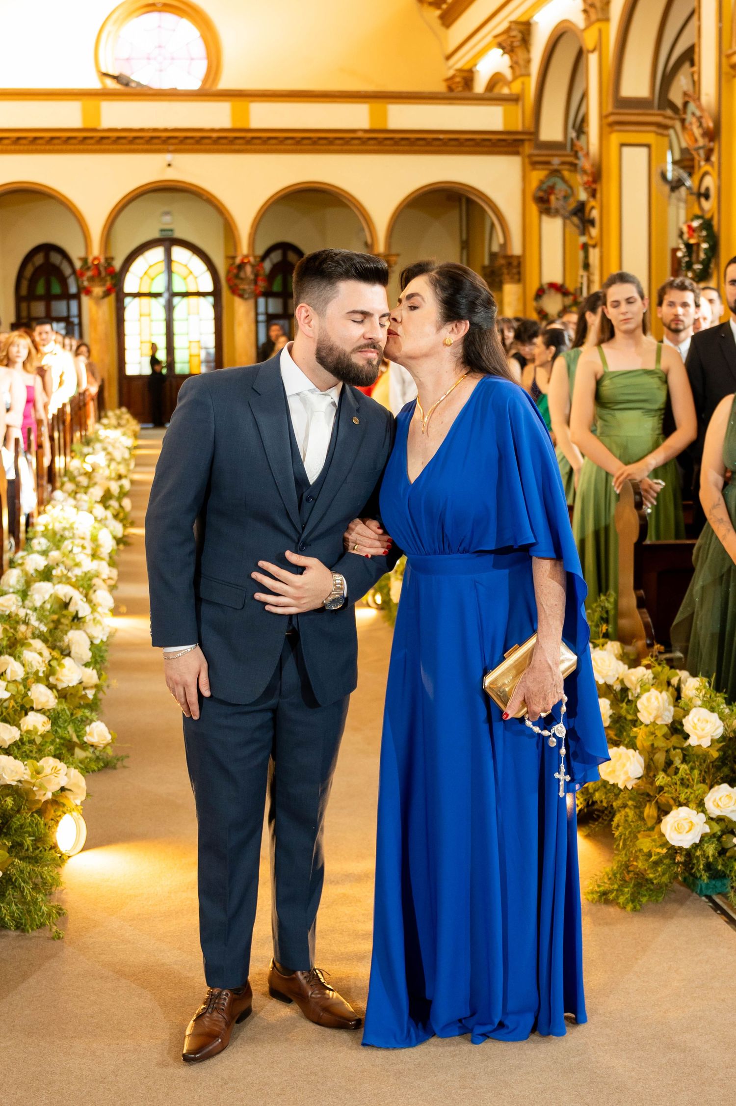 A man in a navy suit and woman in a royal blue gown share a tender moment in an elegant church aisle.