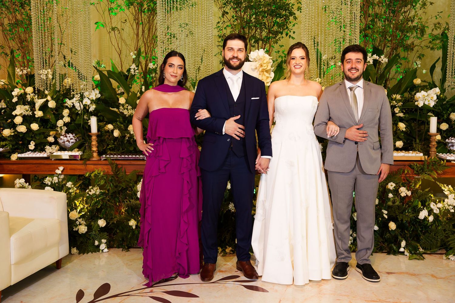 Wedding party of four posing elegantly, bride in white gown, groom in navy suit, guests in purple dress and gray suit.