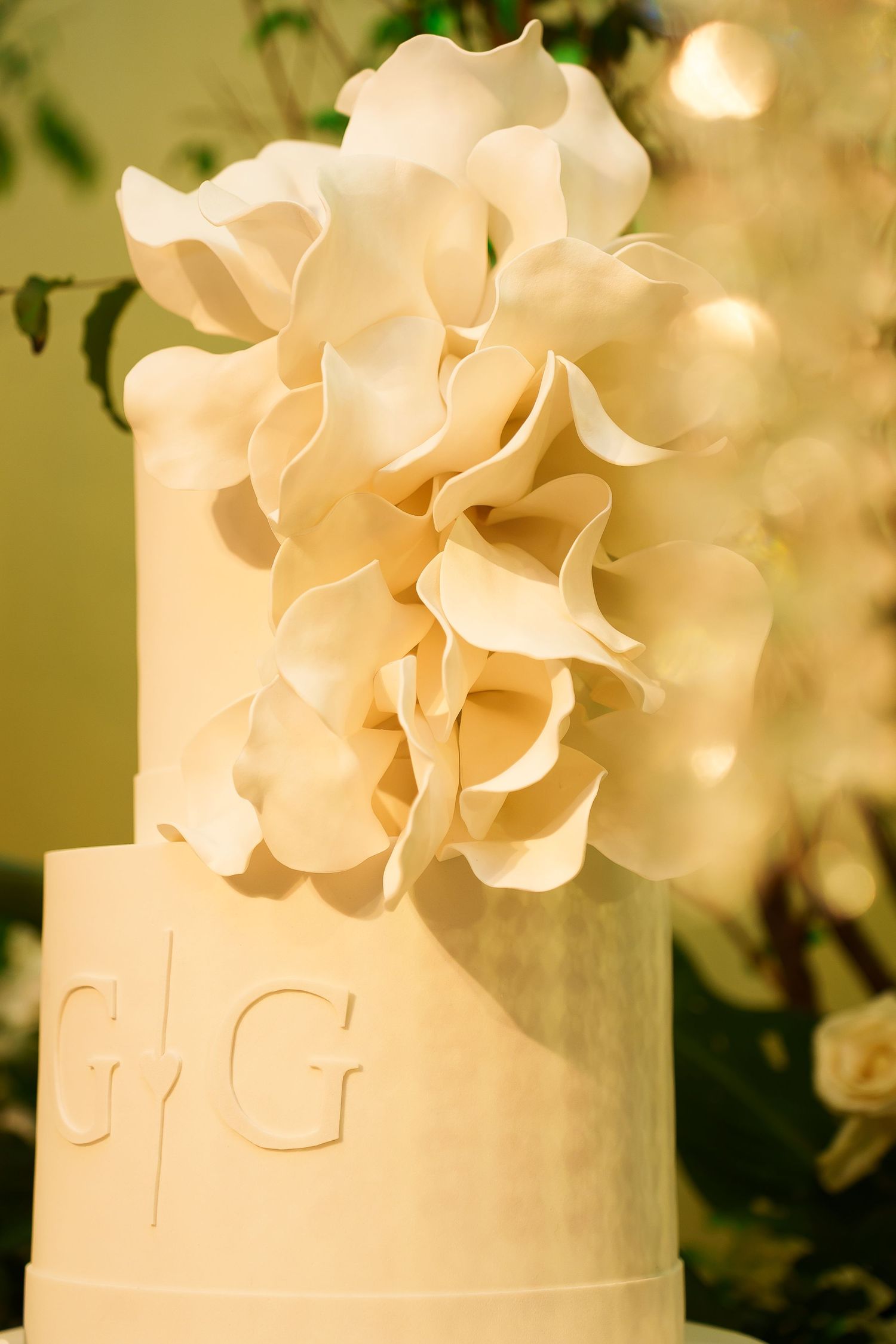 Elegant white wedding cake with sugar flower decorations and monogram GG initials on a tiered fondant design.