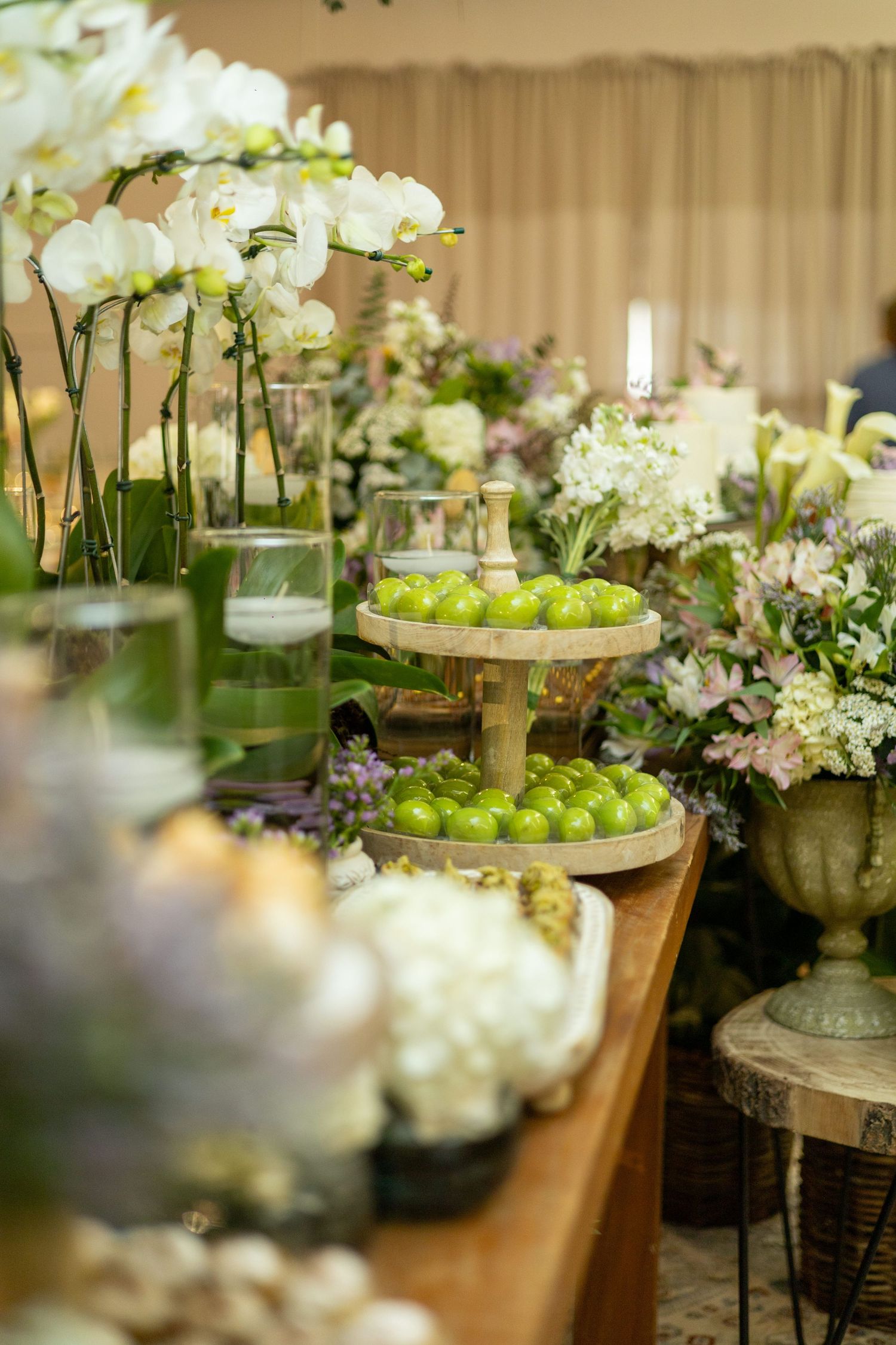 Elegant wedding table display with white orchids, green apples on tiered stand, and lush floral arrangements.