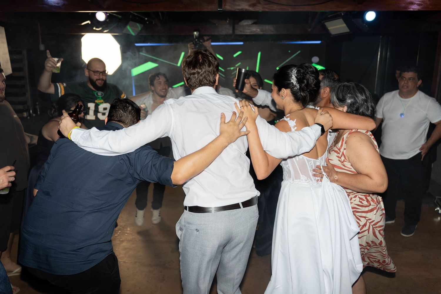 Group of wedding guests dancing together in a circle on the dance floor at a reception party.