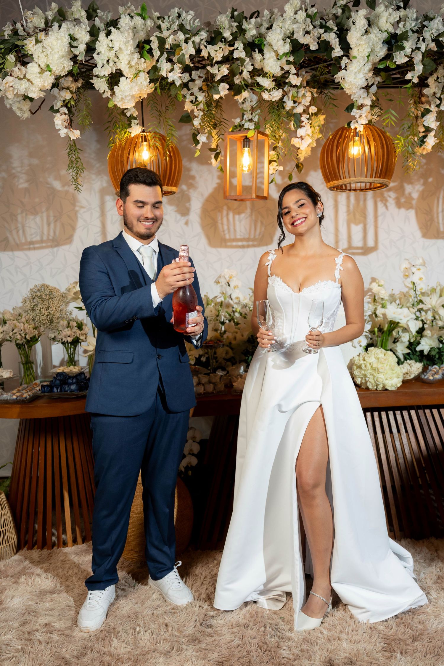 Bride and groom toast with champagne at elegant wedding reception with floral decor and warm pendant lights.