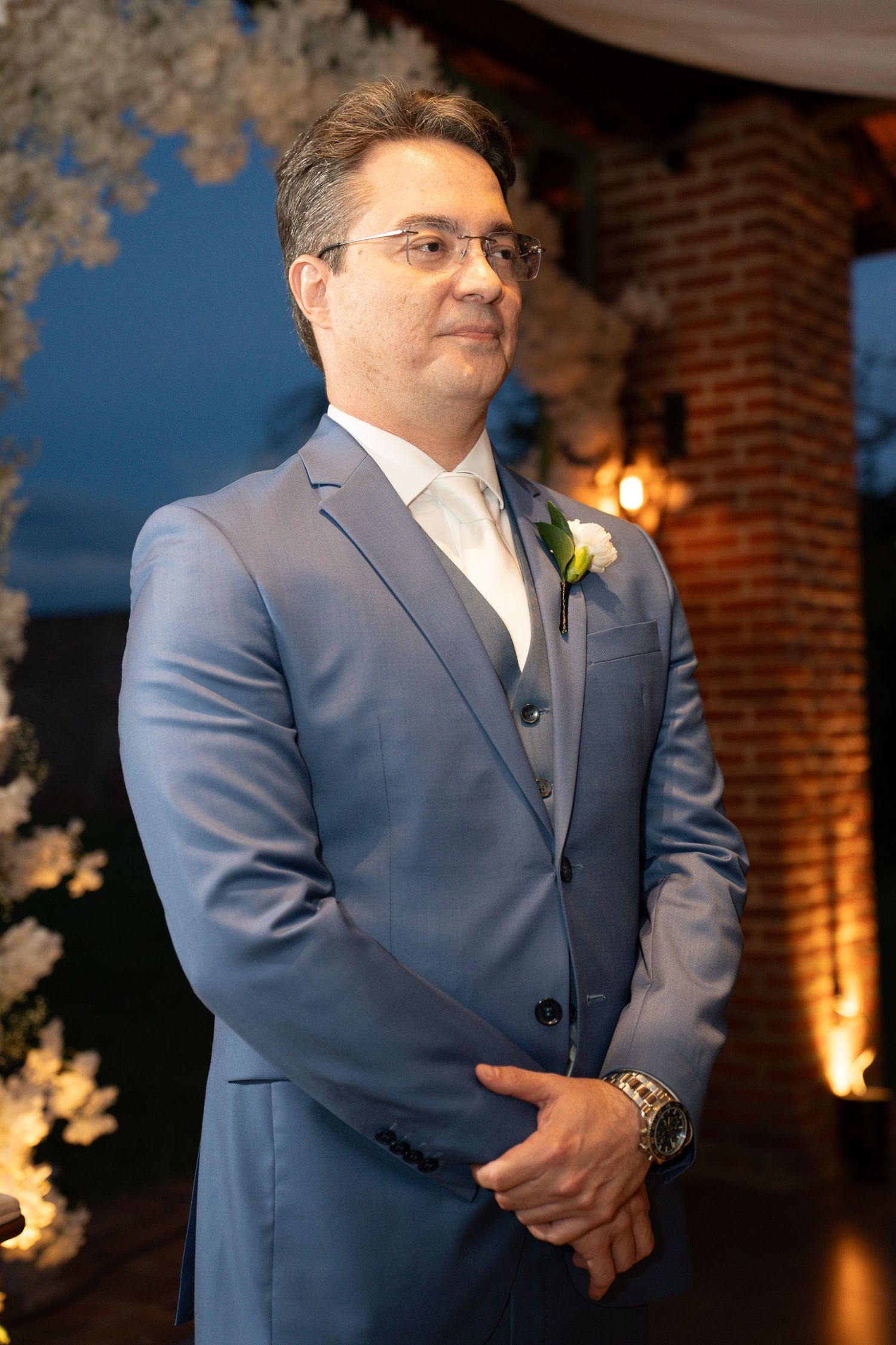 A groom in a blue suit with a boutonniere stands at the altar during an elegant evening wedding ceremony.