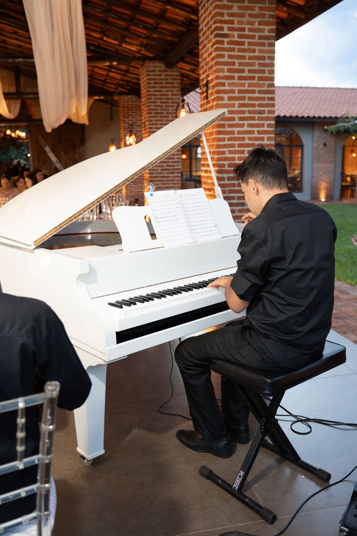 Musician in black attire playing a white grand piano outdoors at an elegant evening event.