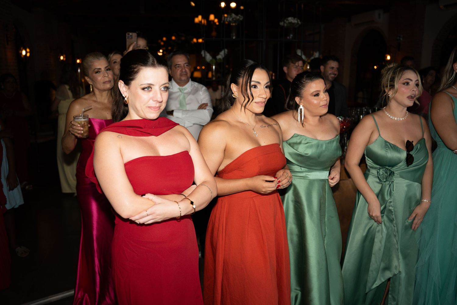 Women in elegant evening gowns in red, orange, and green at a formal event or wedding reception.