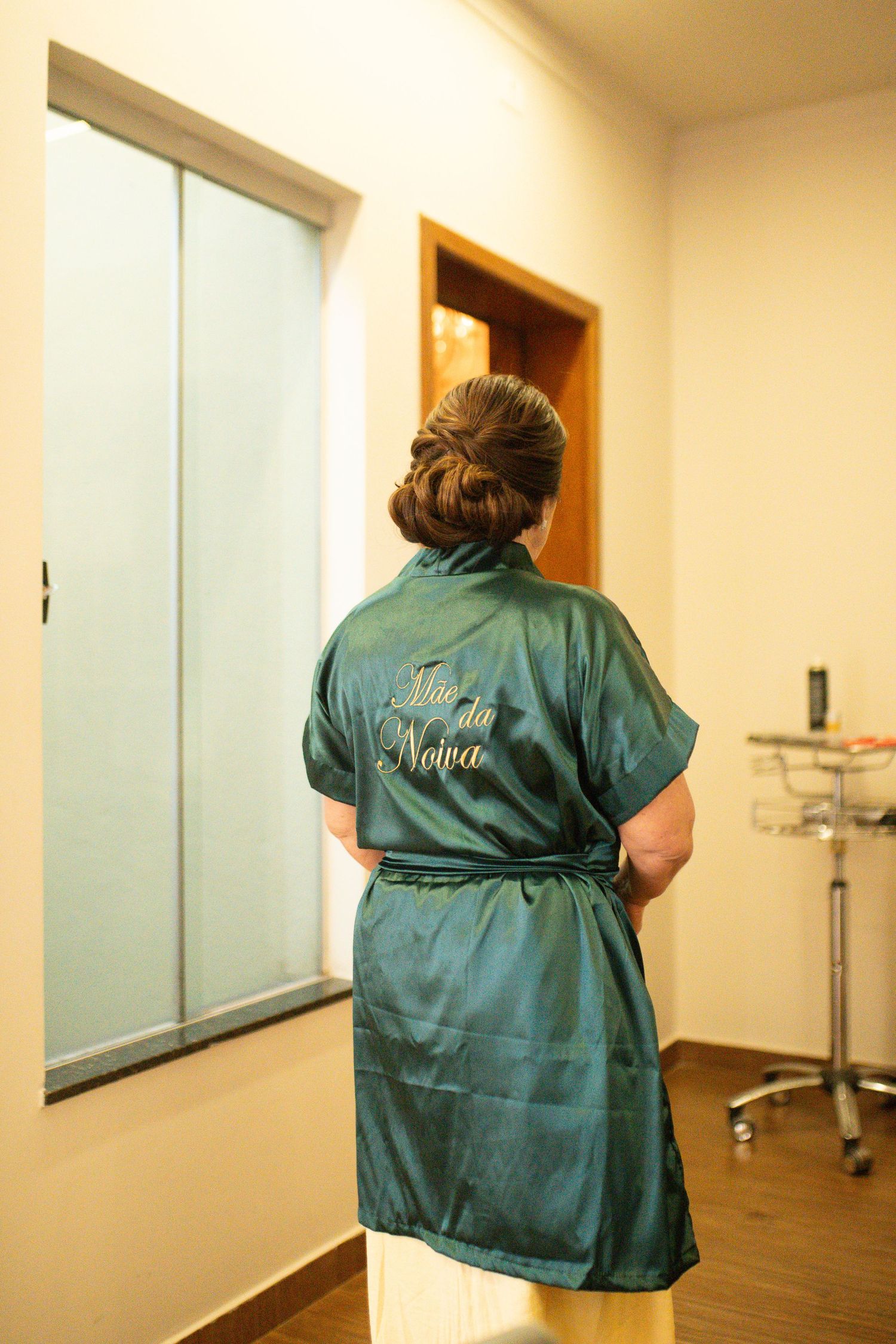 Woman in green satin robe with Portuguese text stands facing away, hair styled in elegant updo.