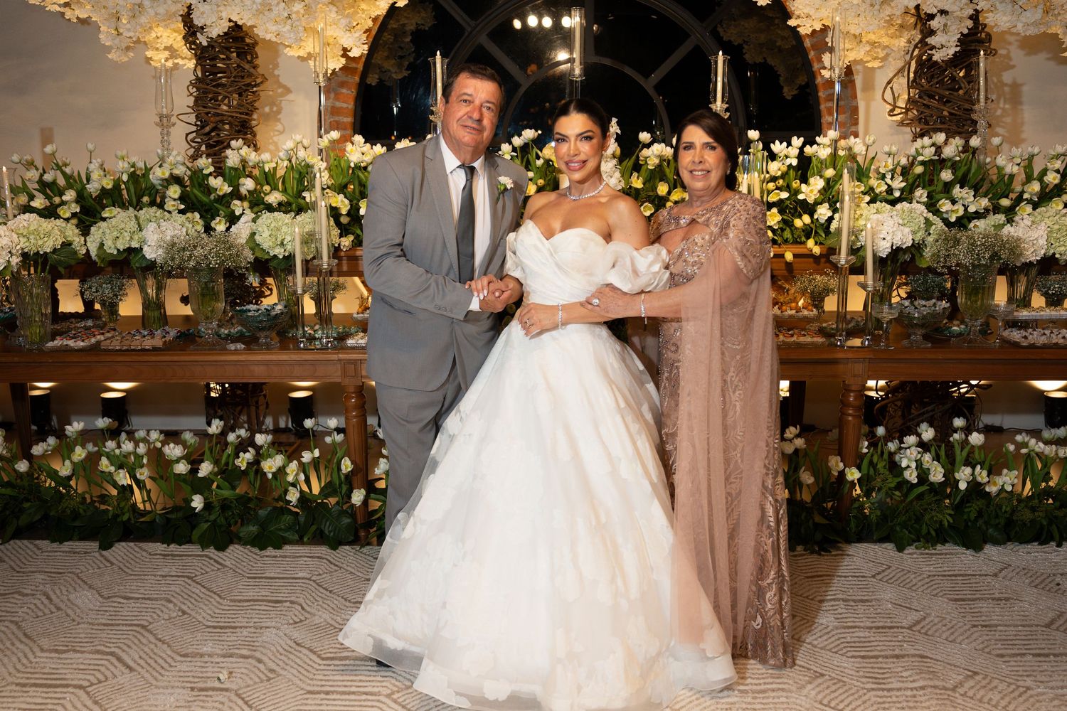 Bride in white ball gown poses with two guests at an elegant floral wedding reception.