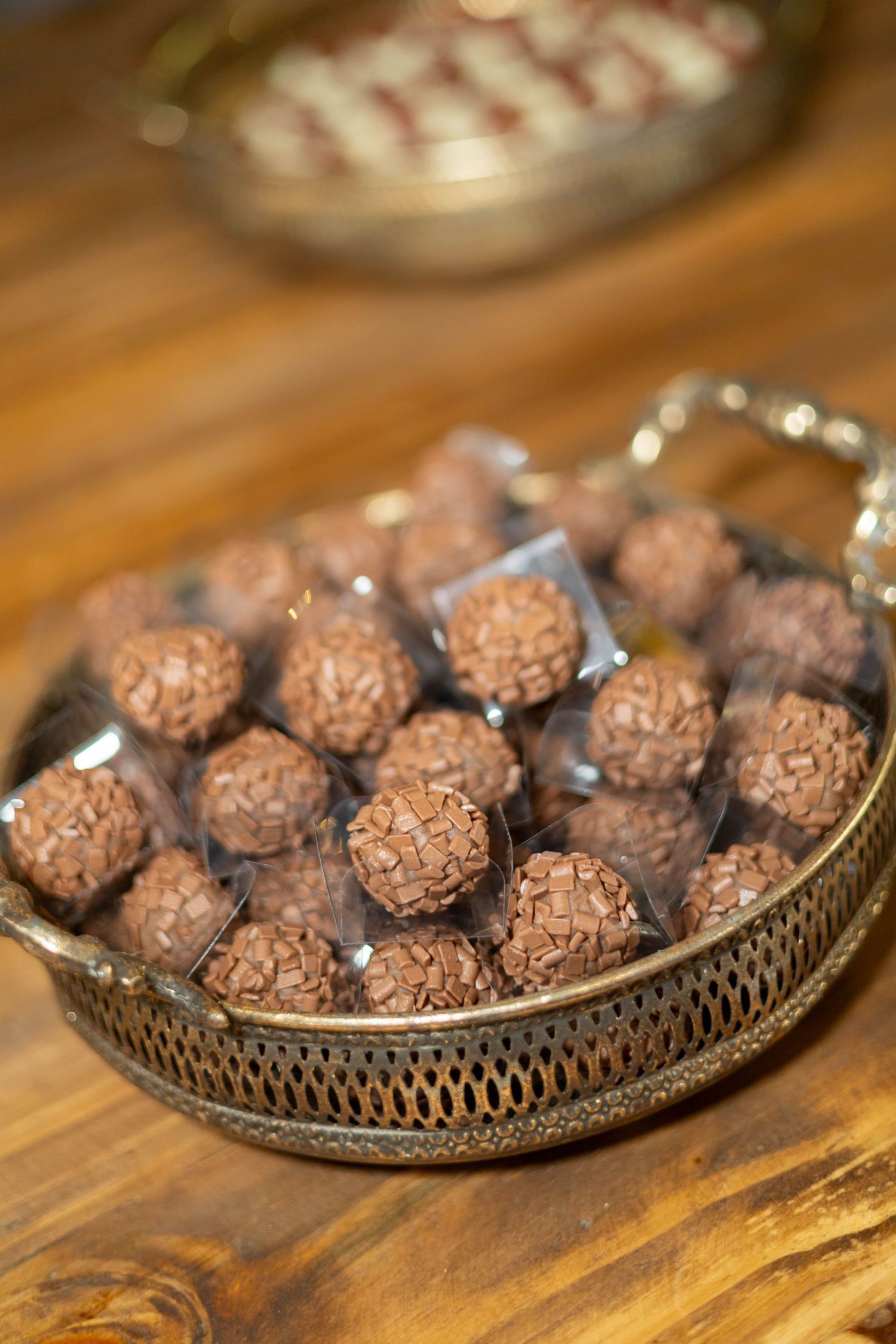 A decorative silver tray filled with chocolate truffle bonbons in clear wrappers on a wooden table.