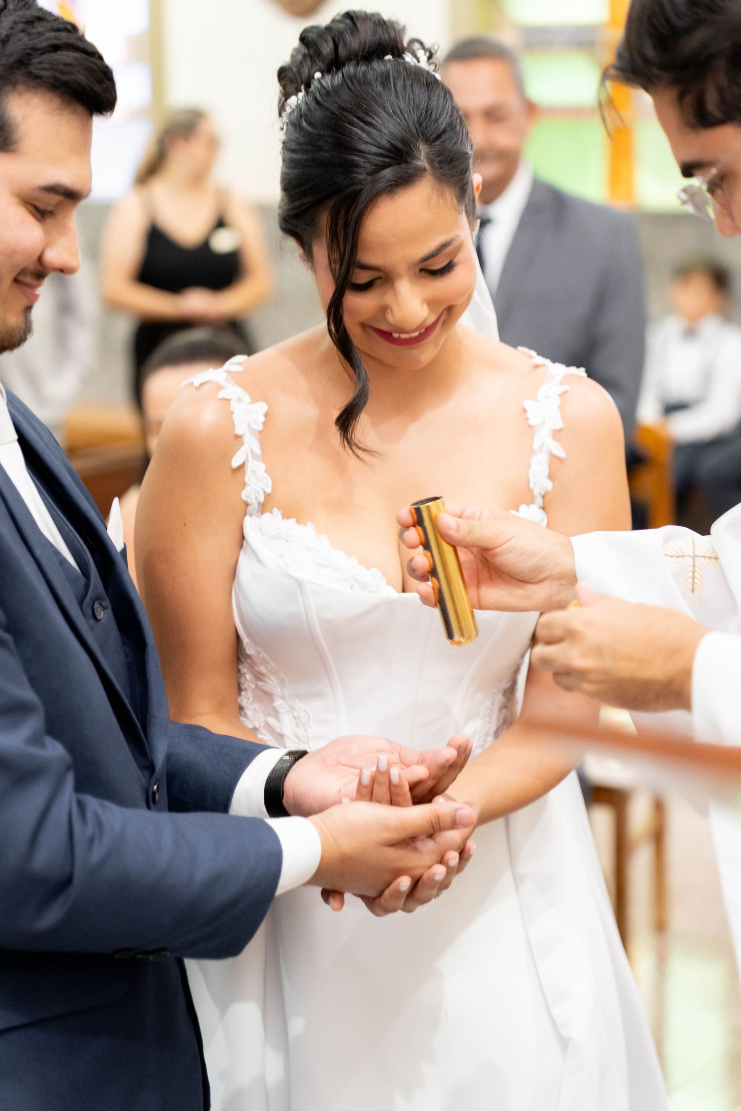 Bride and groom exchange rings during wedding ceremony, bride smiling in white lace gown.