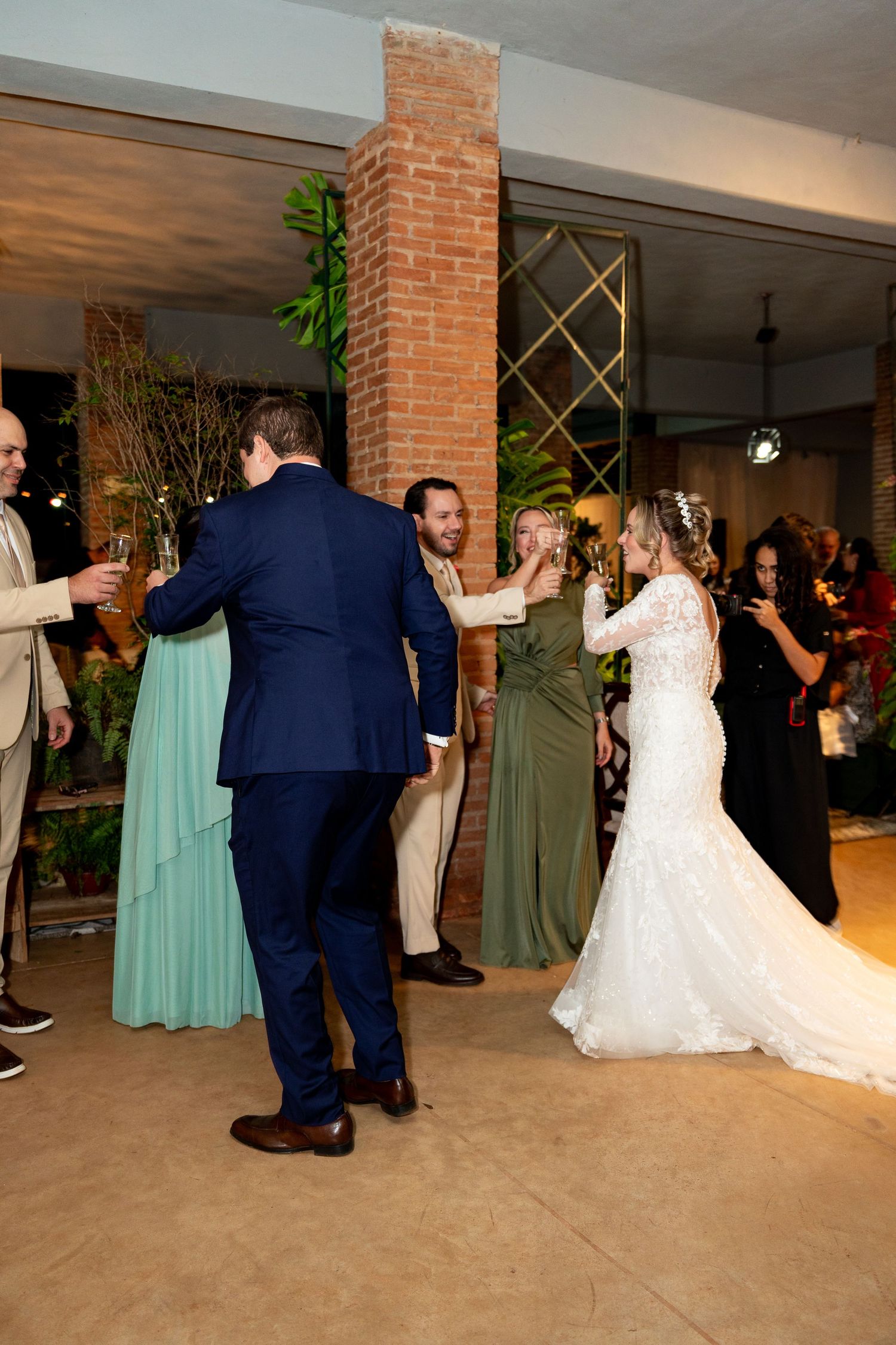 Bride in white lace gown dances with groom in navy suit at elegant indoor wedding reception venue.