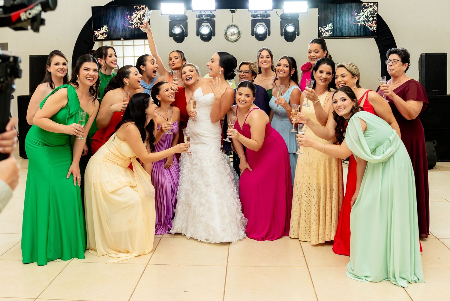 Bride in white gown poses with bridesmaids in colorful dresses at a wedding reception celebration.
