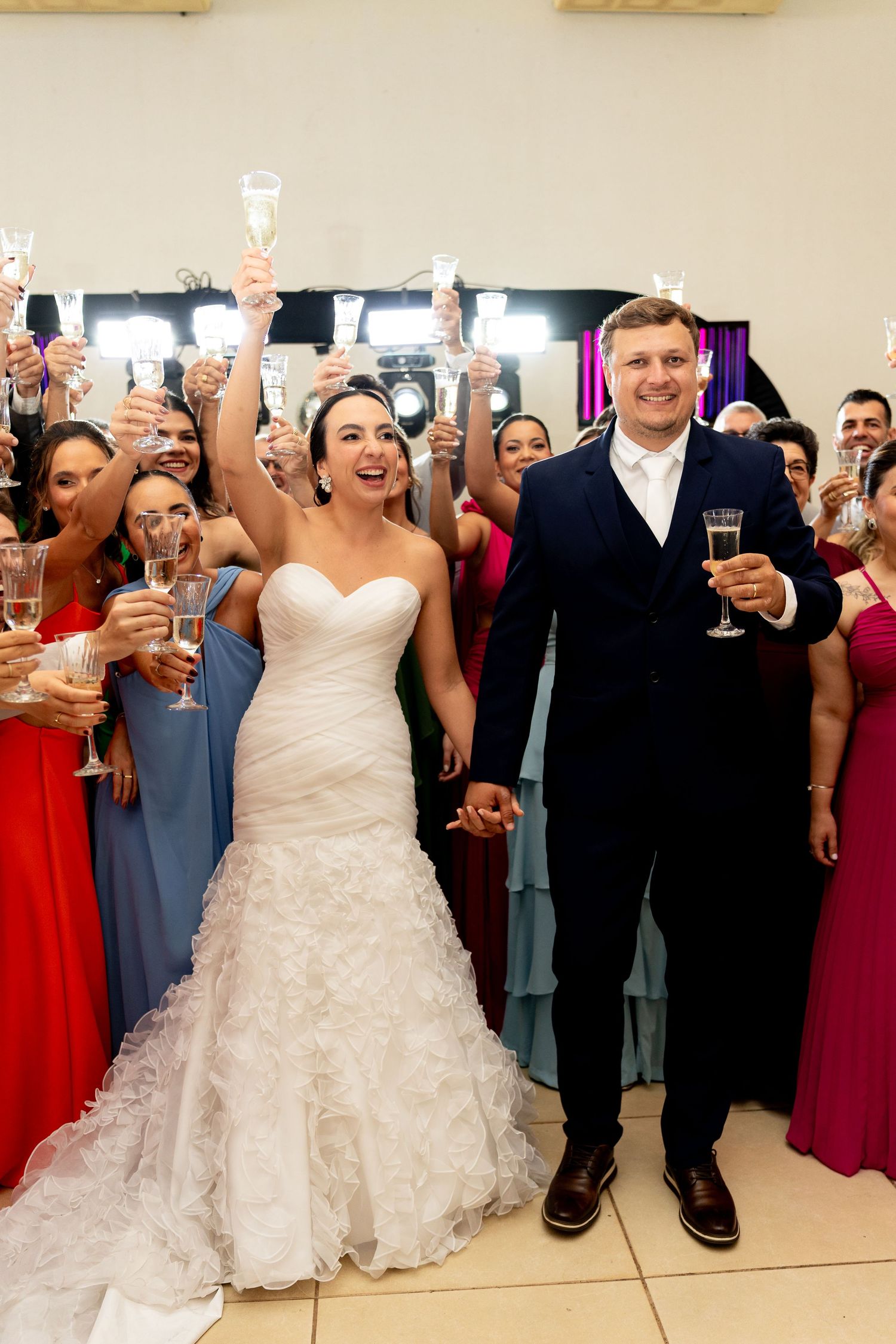 Bride and groom toast with champagne surrounded by guests in colorful formal attire at elegant wedding reception.