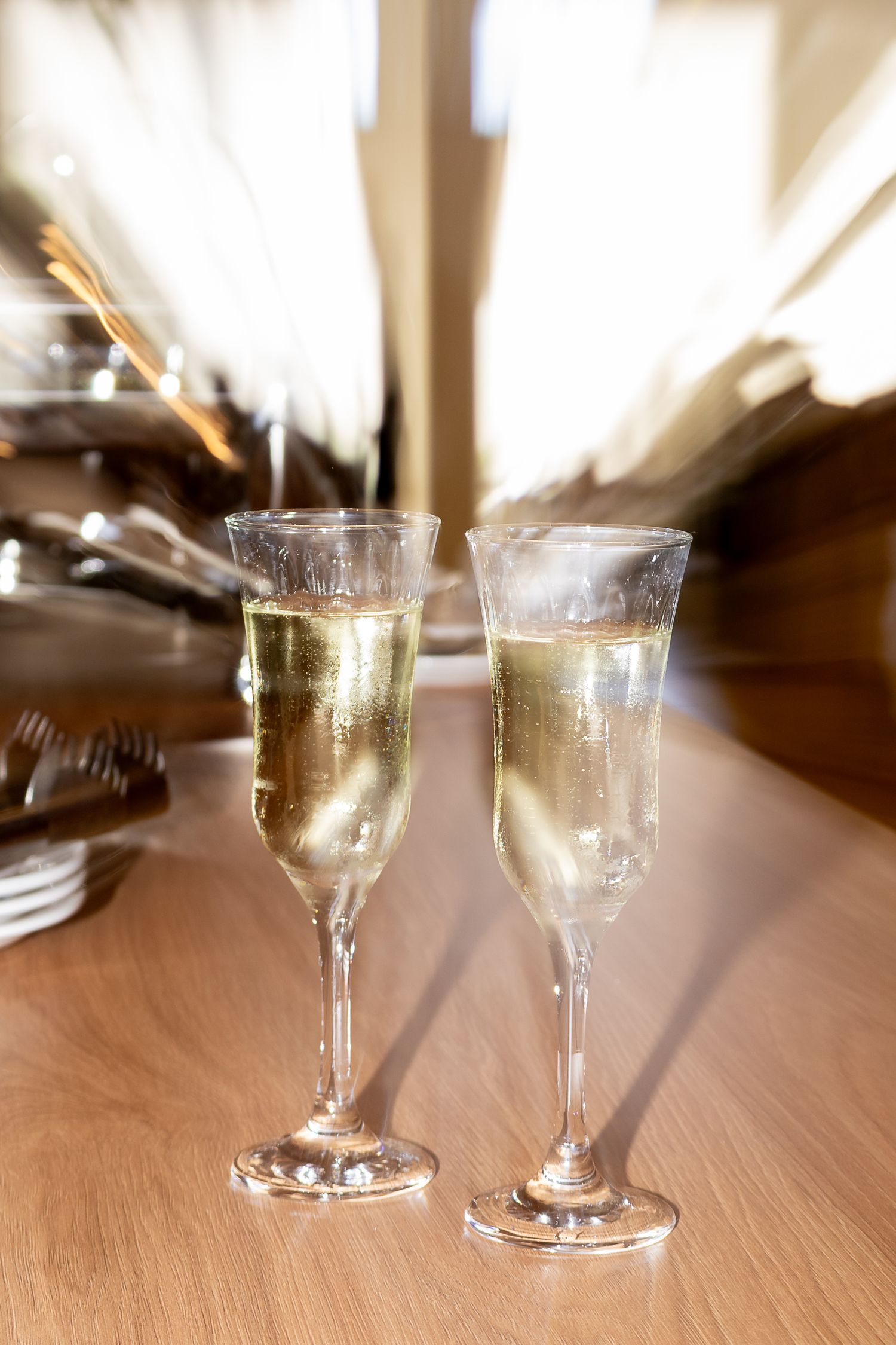 Two elegant champagne flutes filled with sparkling wine on a wooden table at a celebratory event.
