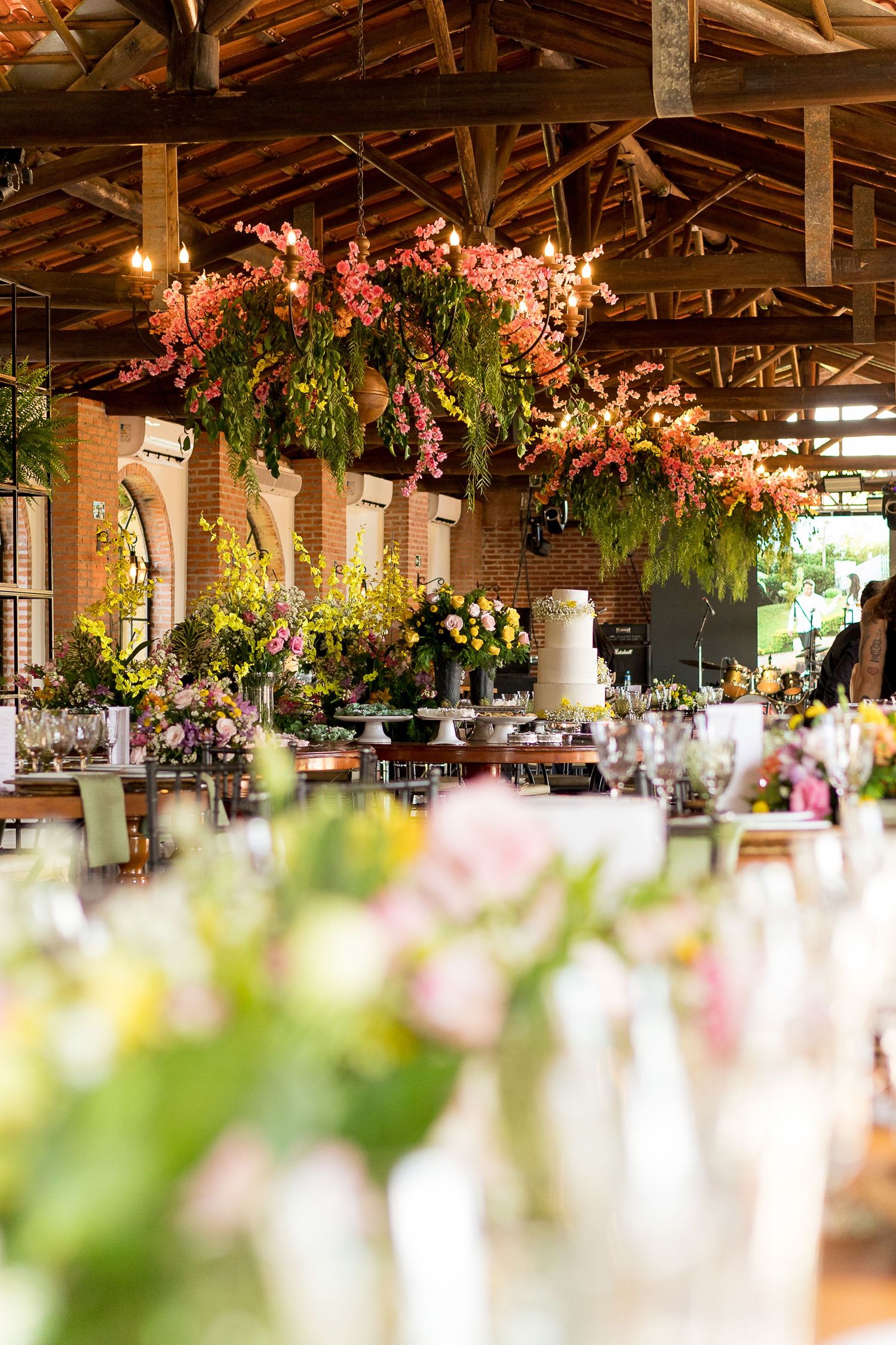 Elegant wedding reception in a rustic barn venue with hanging floral arrangements, string lights, and a tiered cake on display.
