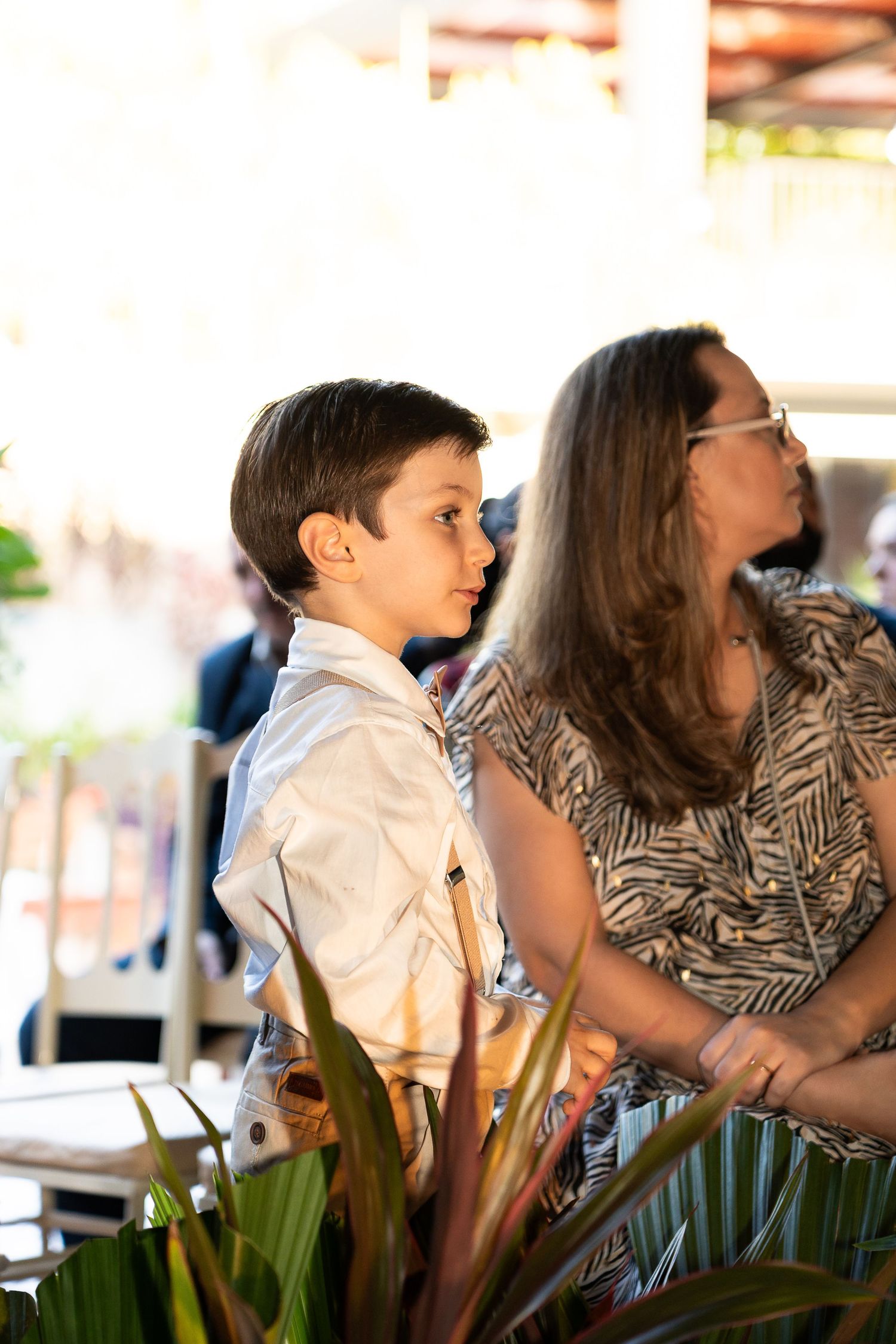 A young boy in a white shirt stands beside a woman in a patterned dress at an outdoor event.