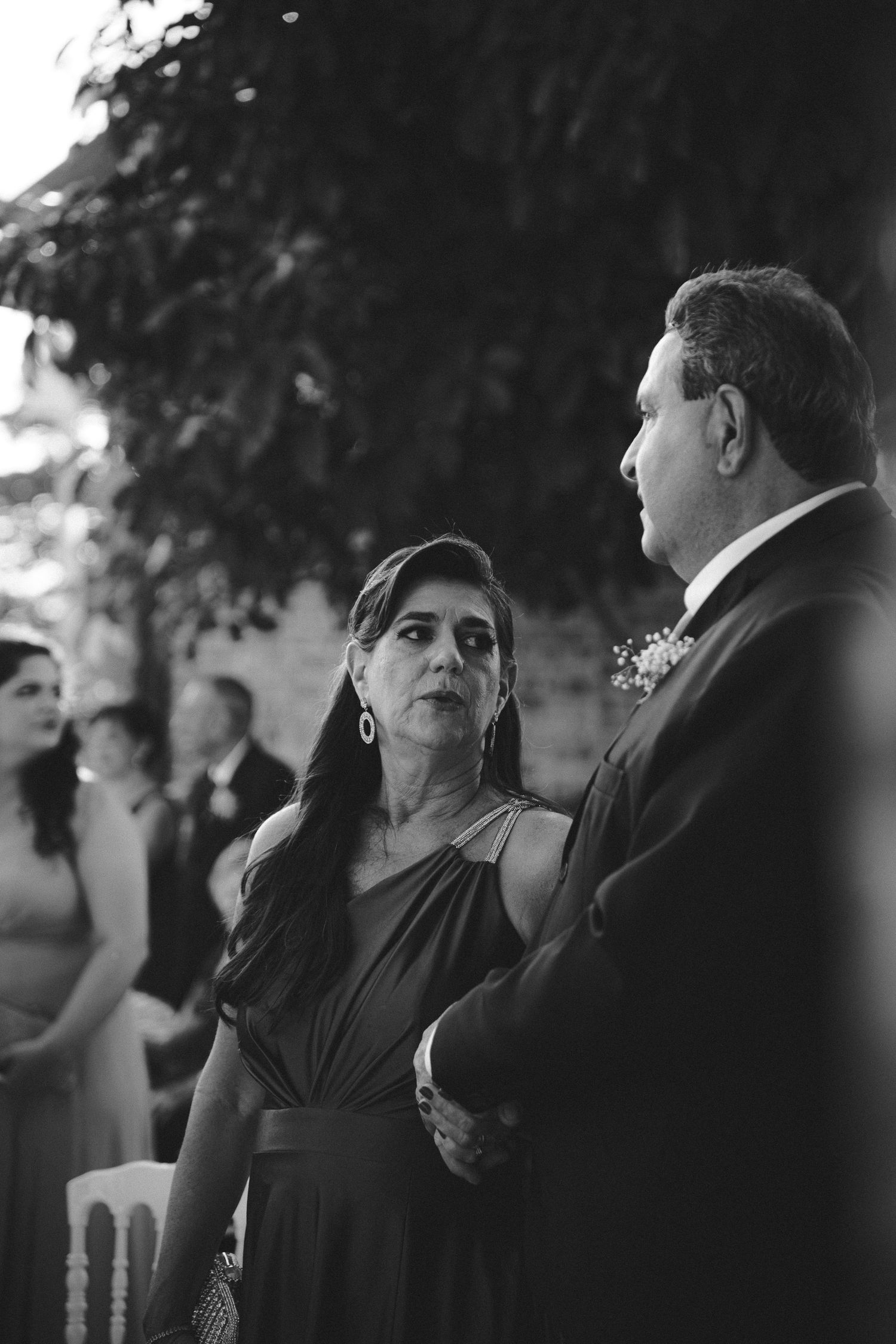 Black and white wedding photo of an elegant woman in a gown exchanging glances with a man in a suit outdoors.
