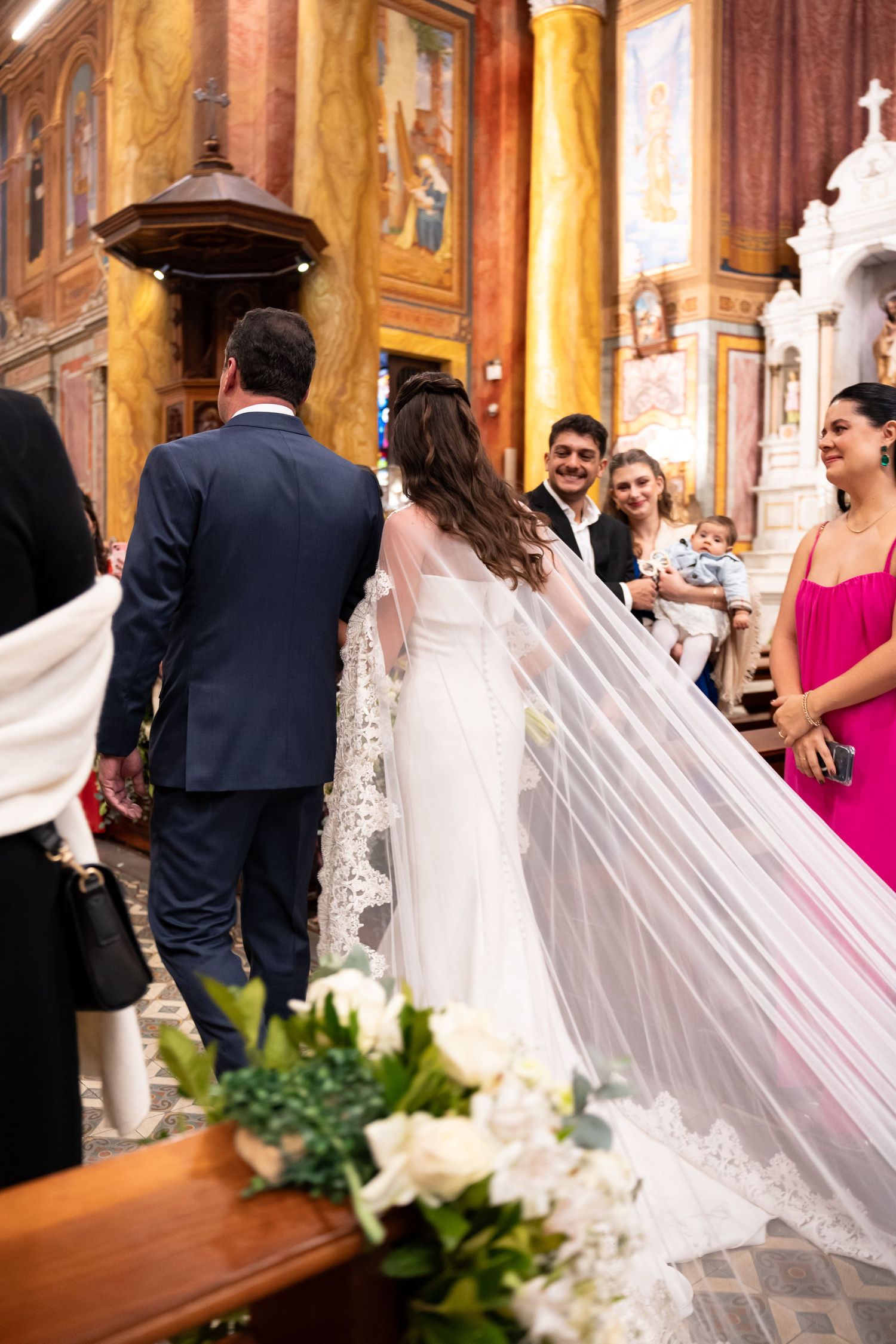 Bride and groom walking down church aisle during wedding ceremony with guests smiling, bride wearing long veil.