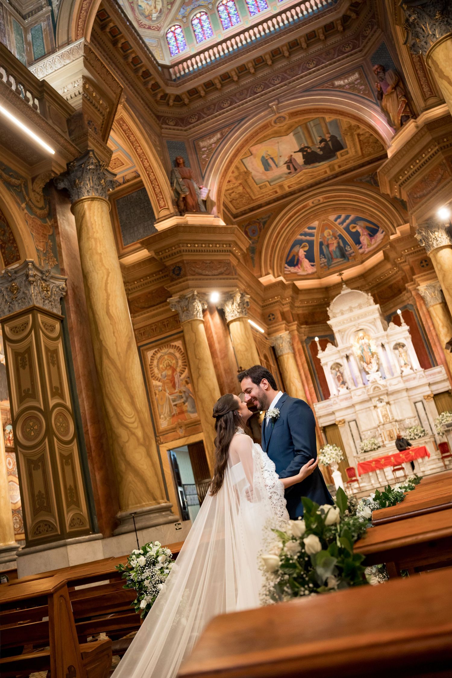 Bride and groom share a romantic kiss at the ornate altar of a stunning historic church during their wedding ceremony.