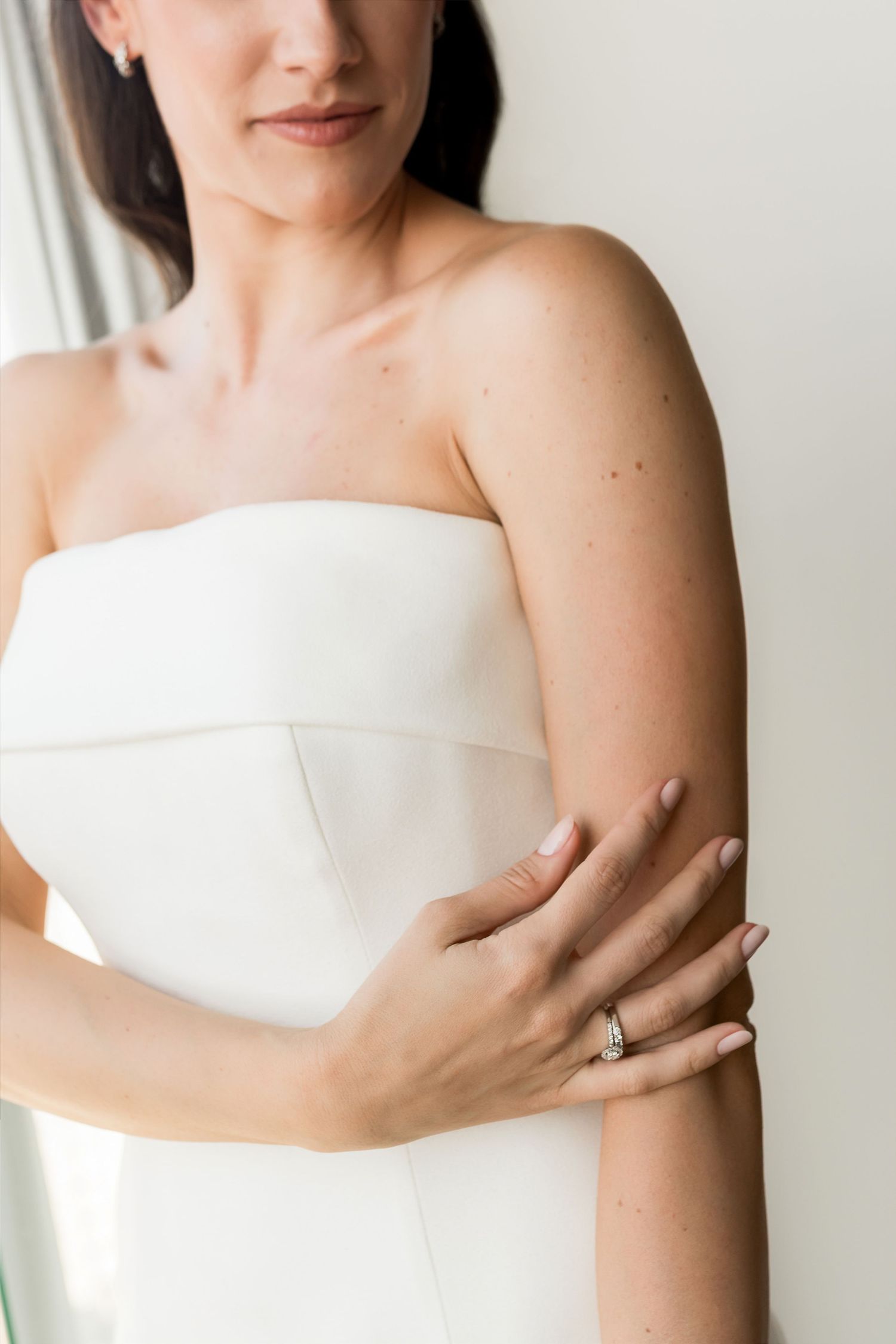 Bride in strapless white wedding gown showcasing elegant diamond engagement ring while posing gracefully.