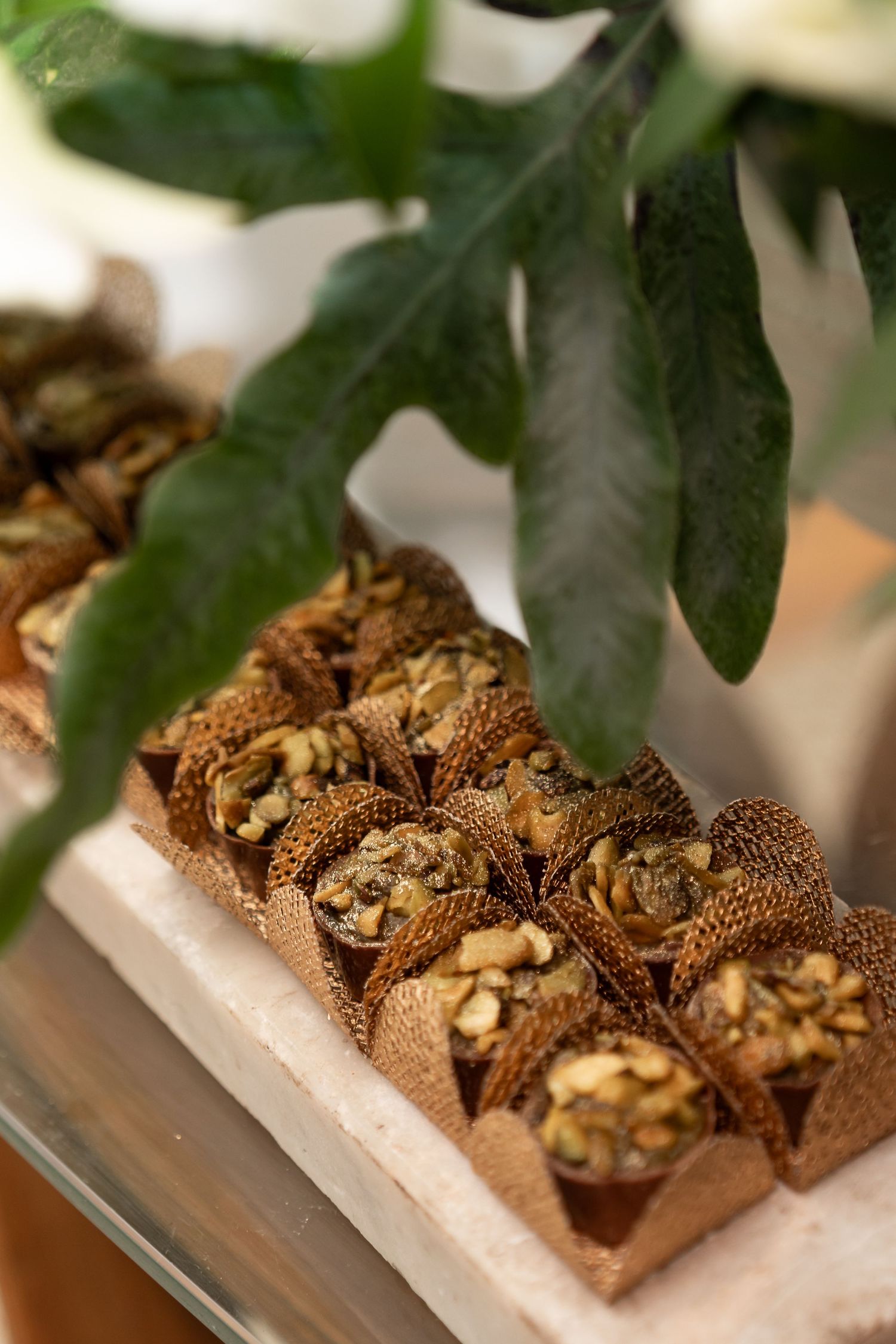 Elegant nut-filled pastry cups in burlap wrappers arranged on a marble tray, garnished with fresh green leaves.