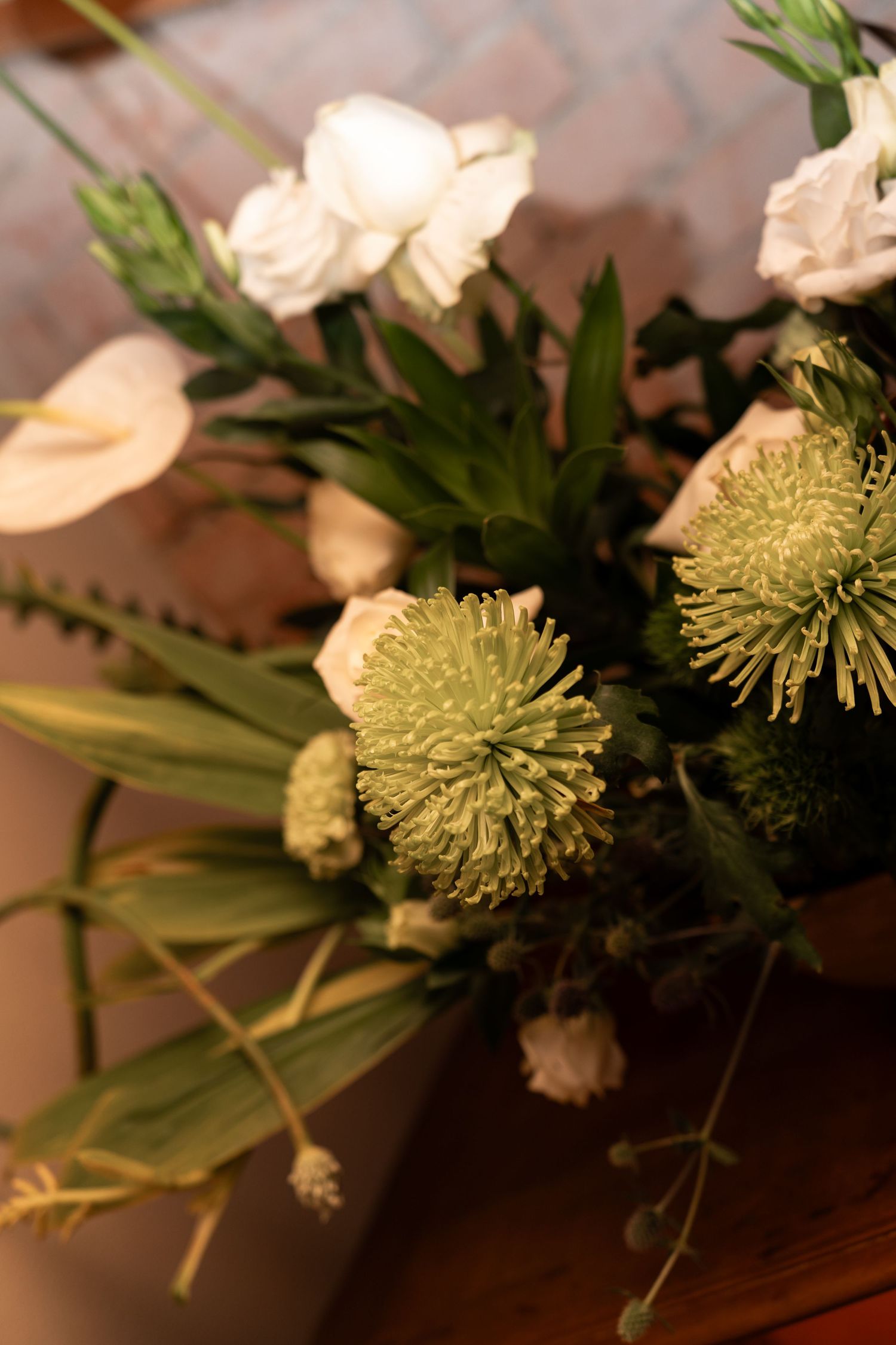 A floral arrangement featuring green chrysanthemums, white roses, calla lilies, and lush foliage on a wooden surface.
