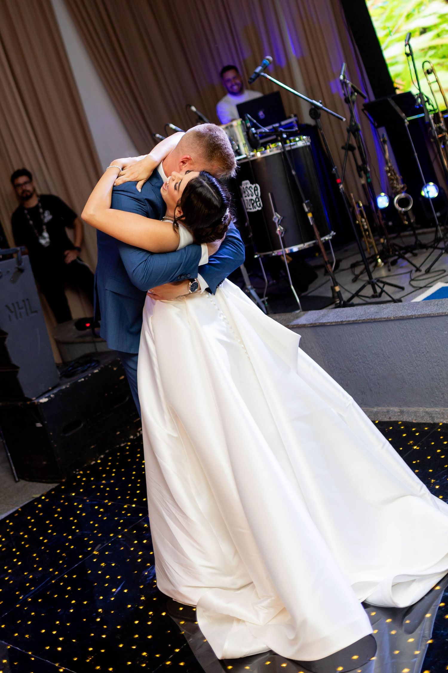 Bride and groom share their first dance embrace at wedding reception with live band performing on stage in background.