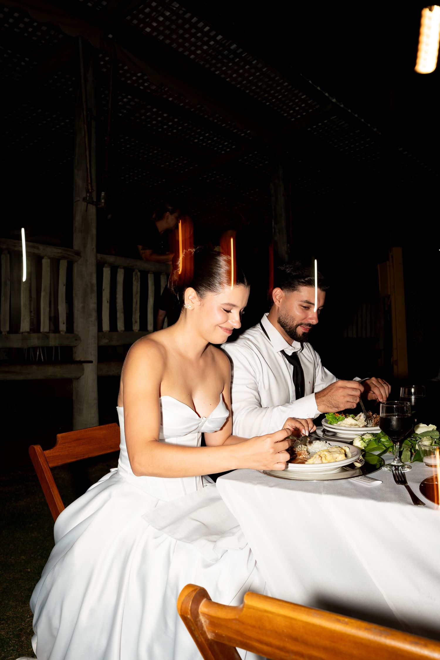 Bride and groom share a romantic candlelit dinner at their wedding reception, dressed in white gown and suit.