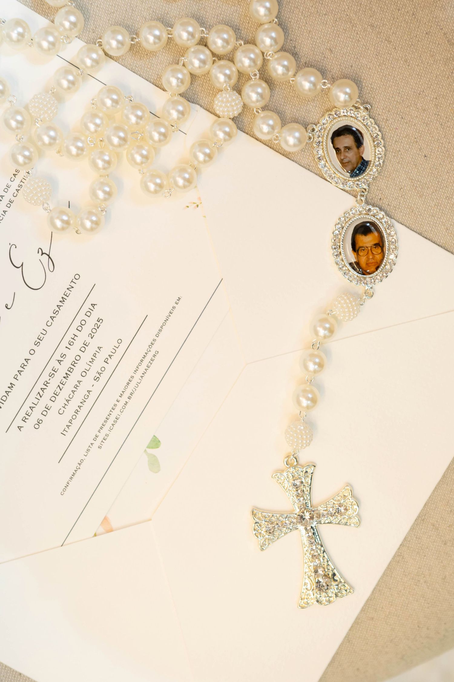 Pearl rosary with photo lockets and cross resting on wedding invitation for a religious ceremony.