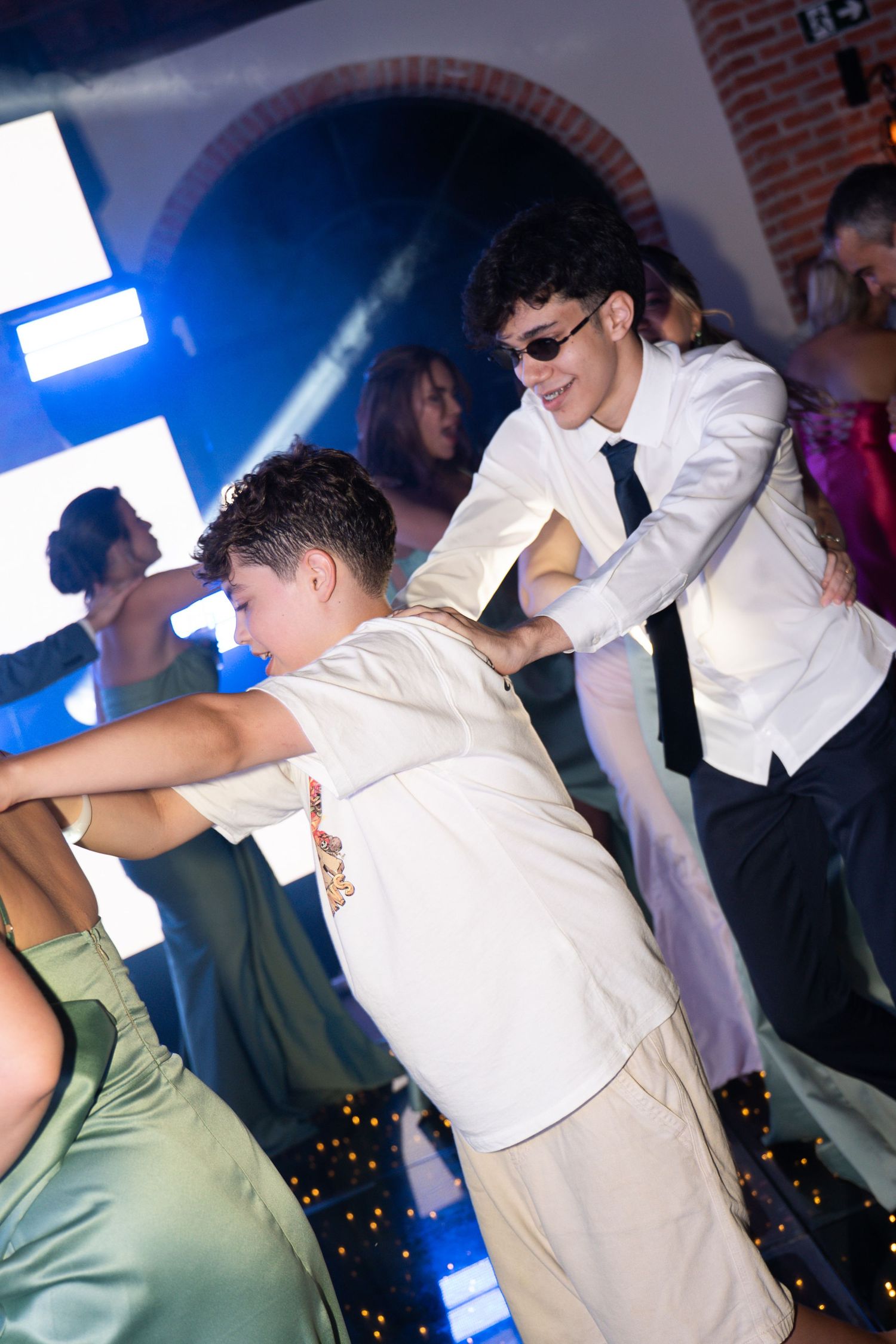 Teenagers dancing at a formal prom event under colorful lights on a decorated dance floor.