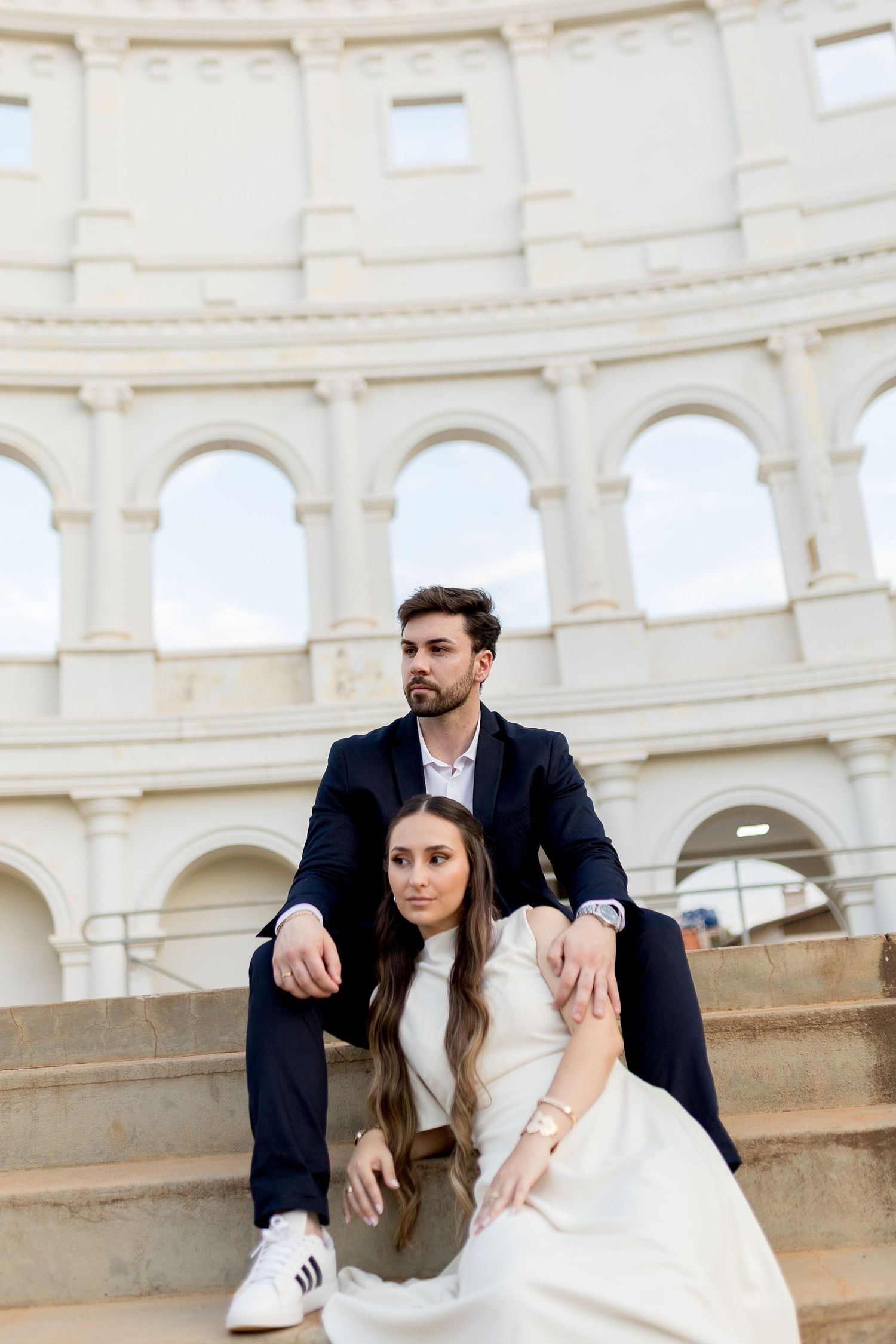 Elegant couple in formal attire sitting on steps of the Colosseum in Rome, Italy.