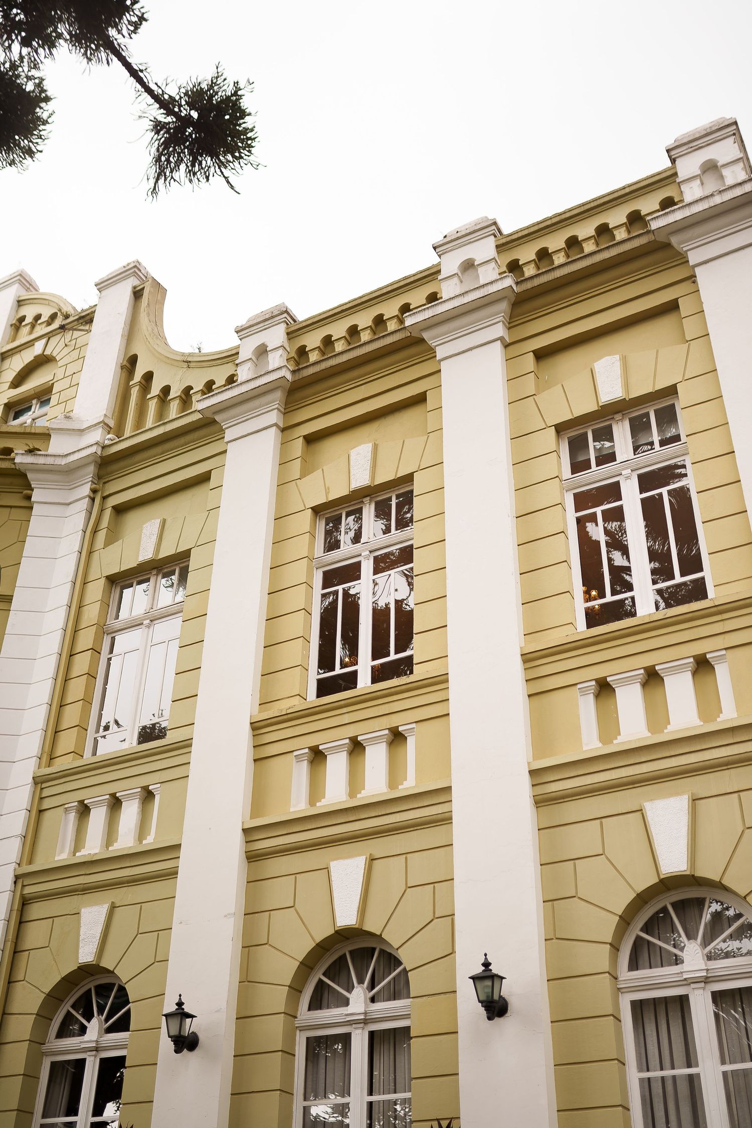 Yellow and white neoclassical building facade with arched windows, decorative pilasters, and ornate cornice details.