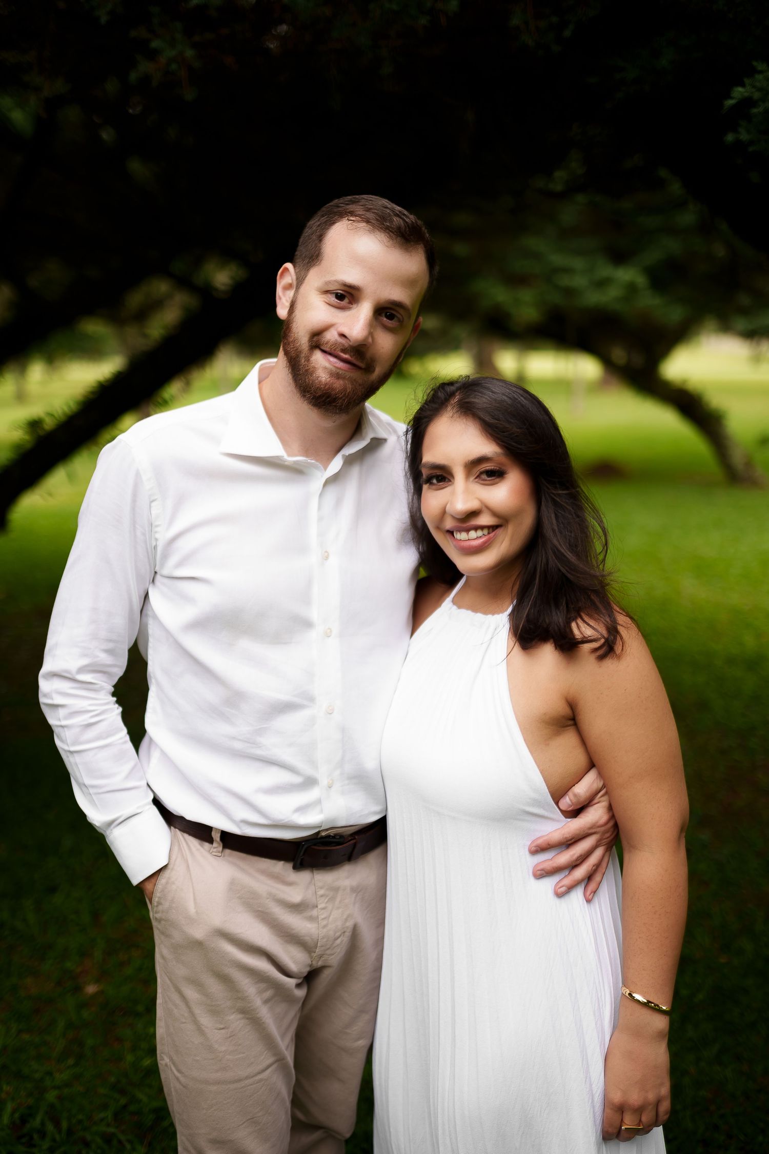 Smiling couple in coordinating white outfits embracing outdoors during an engagement photo session.