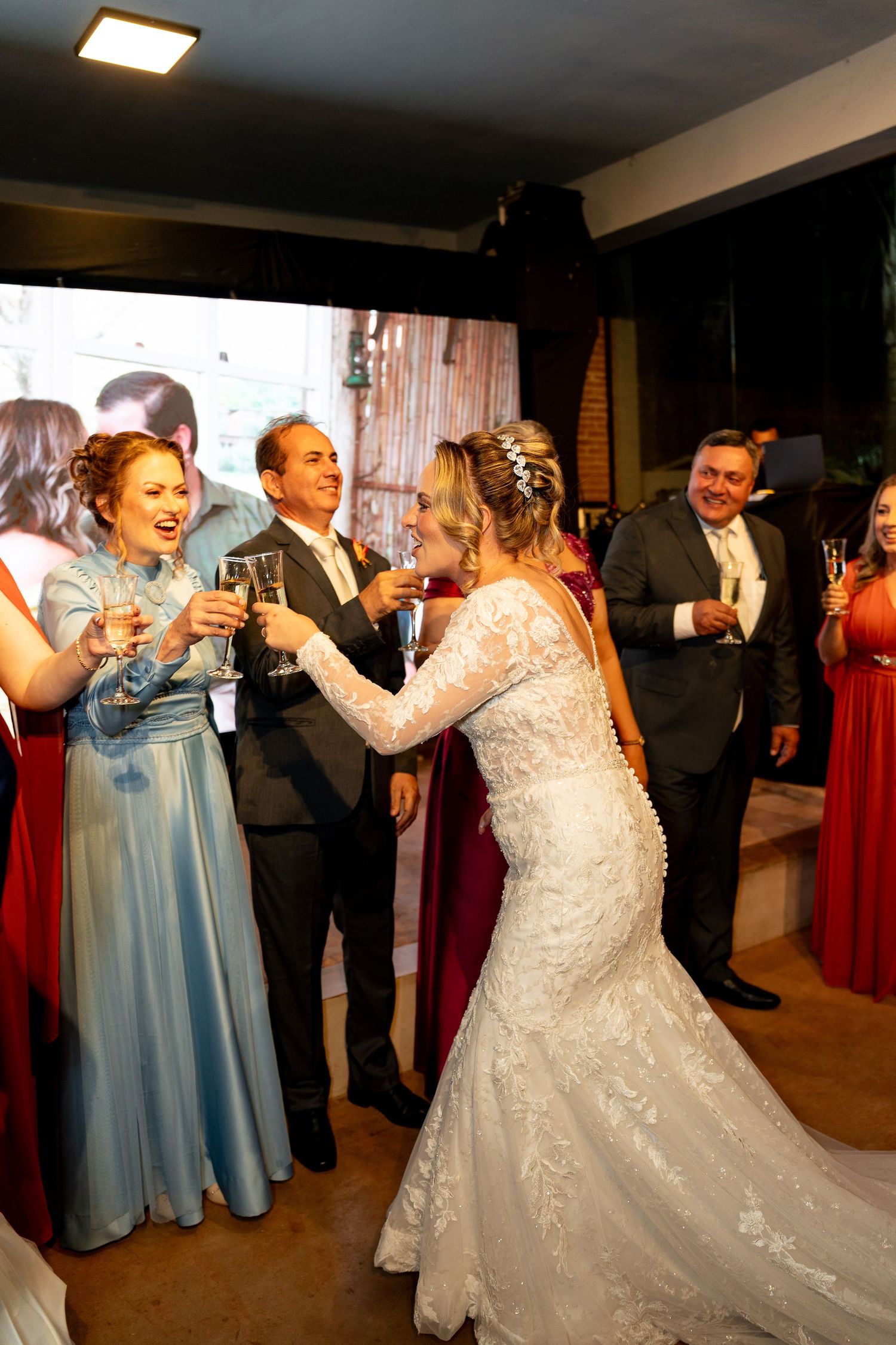 Bride in lace gown toasting champagne with bridesmaids in red and blue dresses at elegant wedding reception.