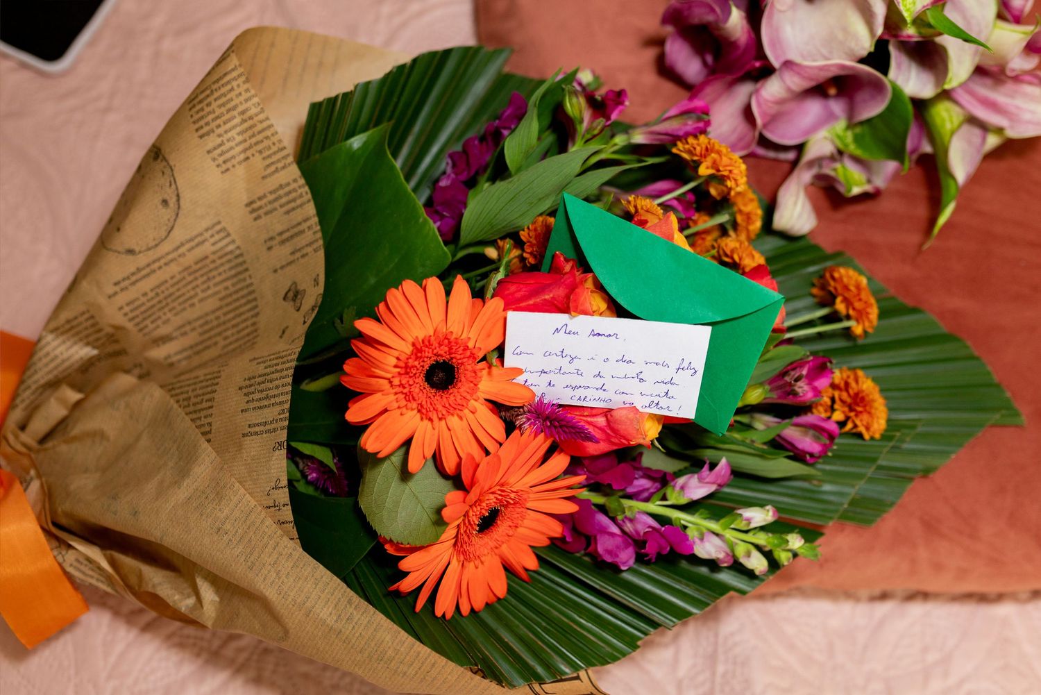 Colorful bouquet of orange gerberas, purple flowers, wrapped in kraft paper with a handwritten green card note.