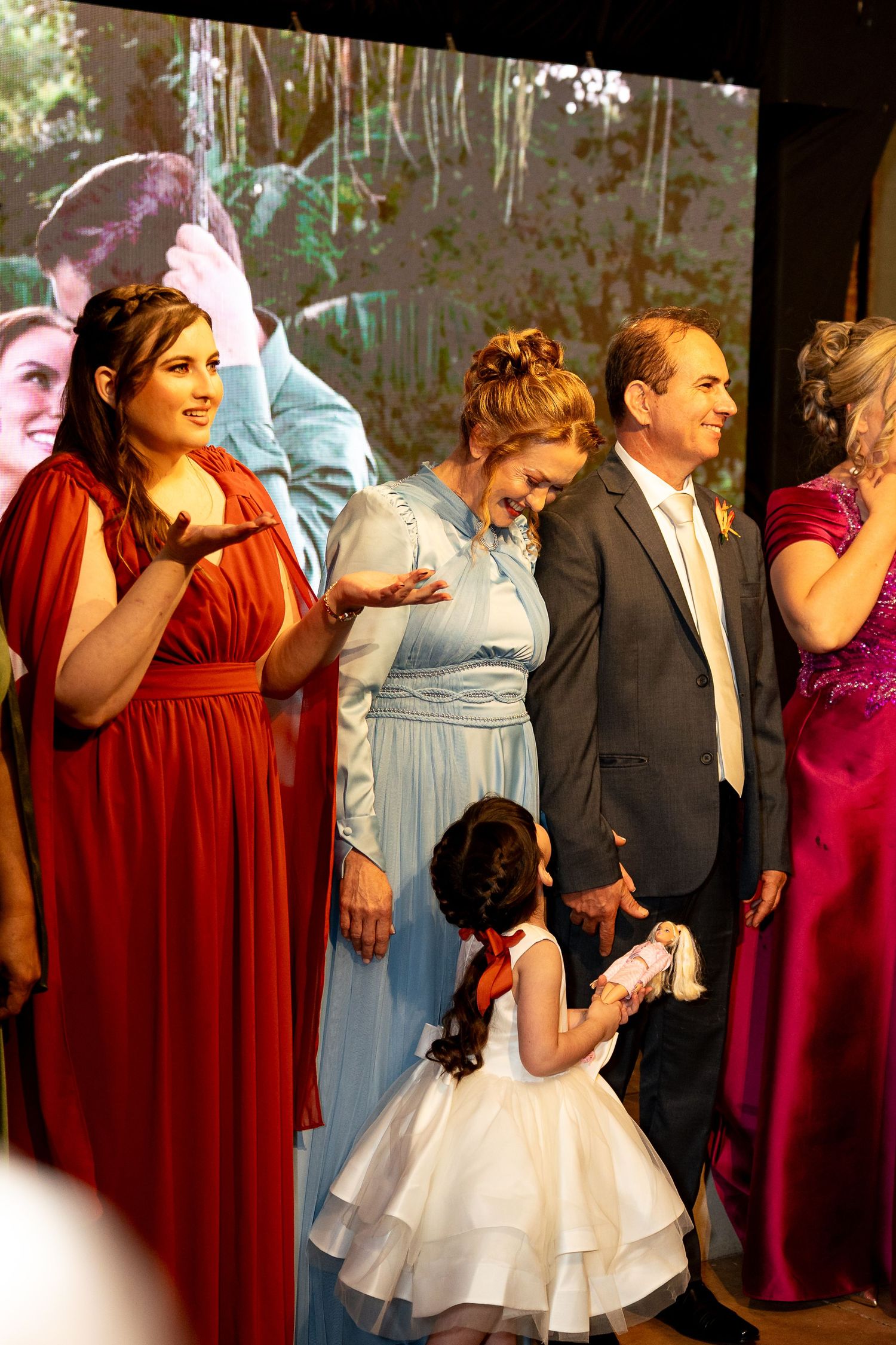 Wedding party in formal attire, bridesmaids in red and blue gowns, with a flower girl in white dress.