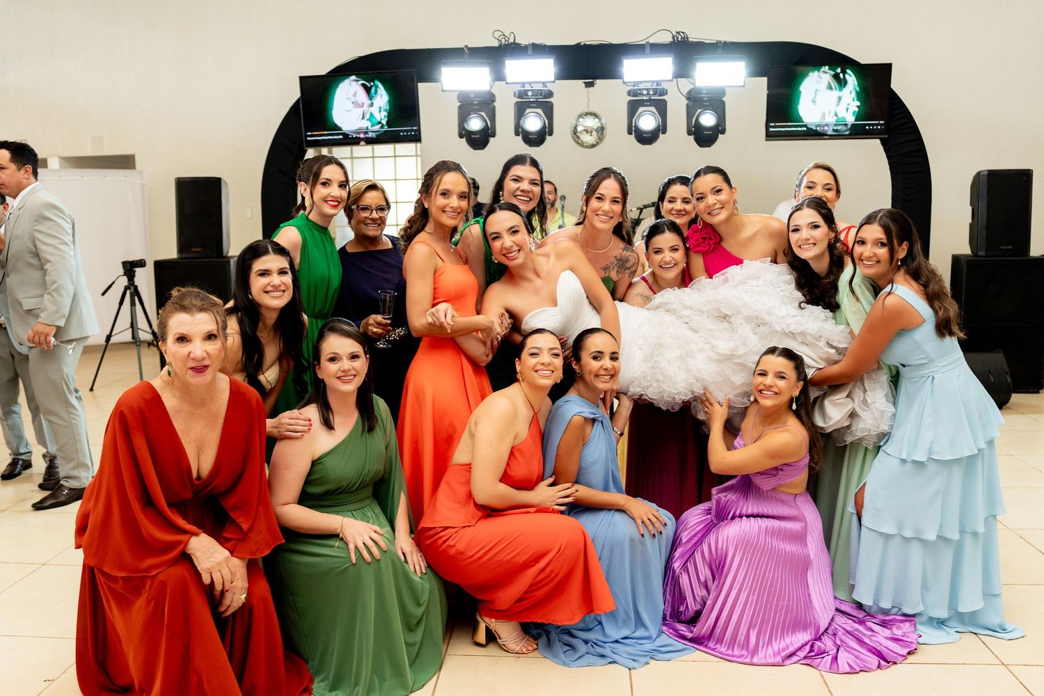 Bride in white gown poses with colorful bridesmaids in rainbow dresses at elegant wedding reception.