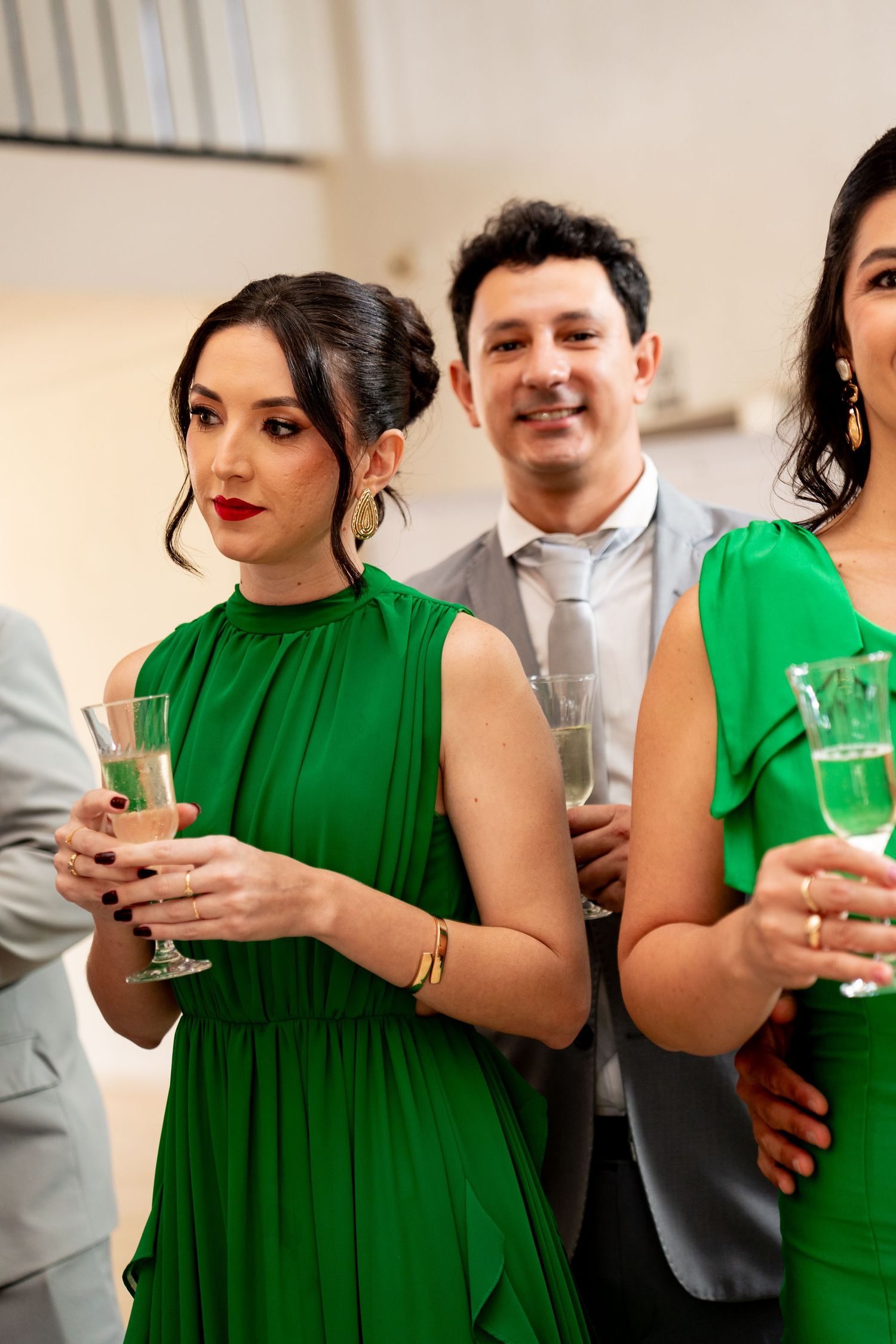 Elegant guests in green dresses holding champagne glasses at a formal event or wedding reception.